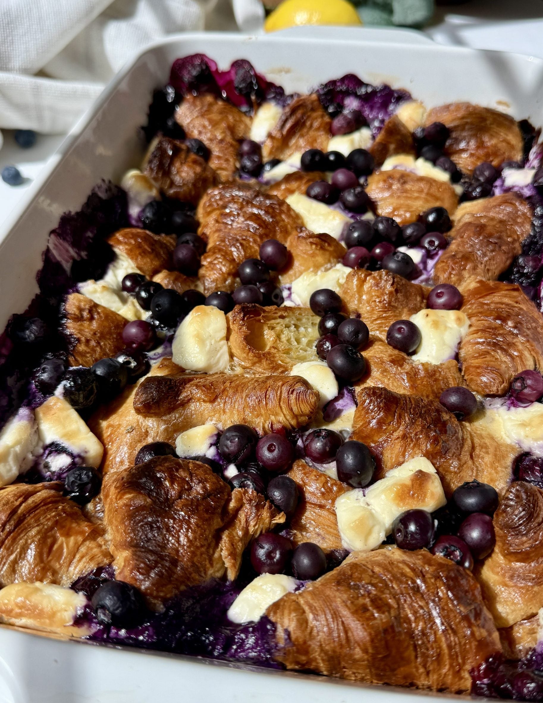 Blueberry lemon croissant bake topped with fresh blueberries and powdered sugar in a white baking dish