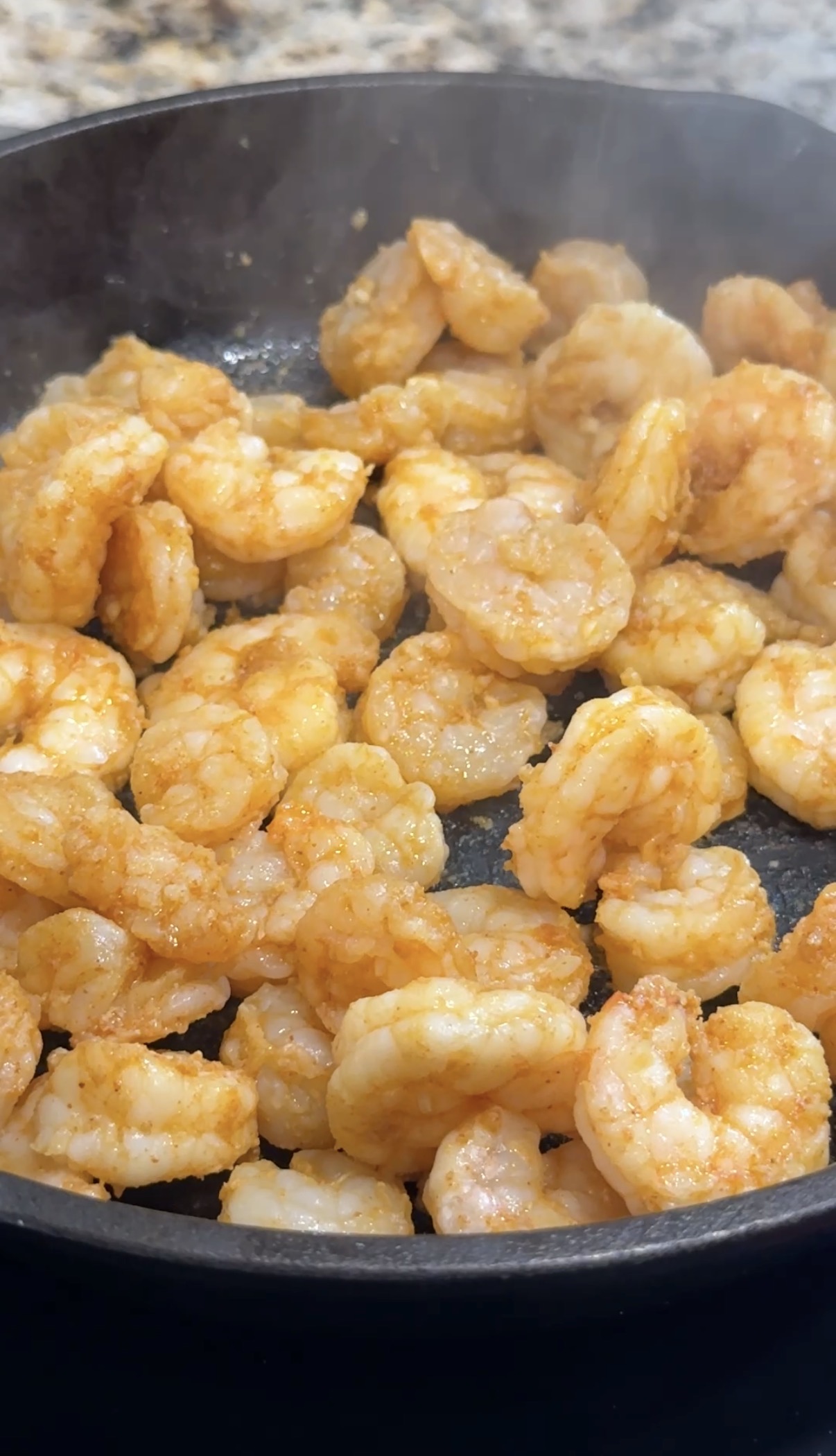 Close-up of seasoned shrimp being cooked in a pan, with steam rising and the shrimp turning golden orange as they sauté.