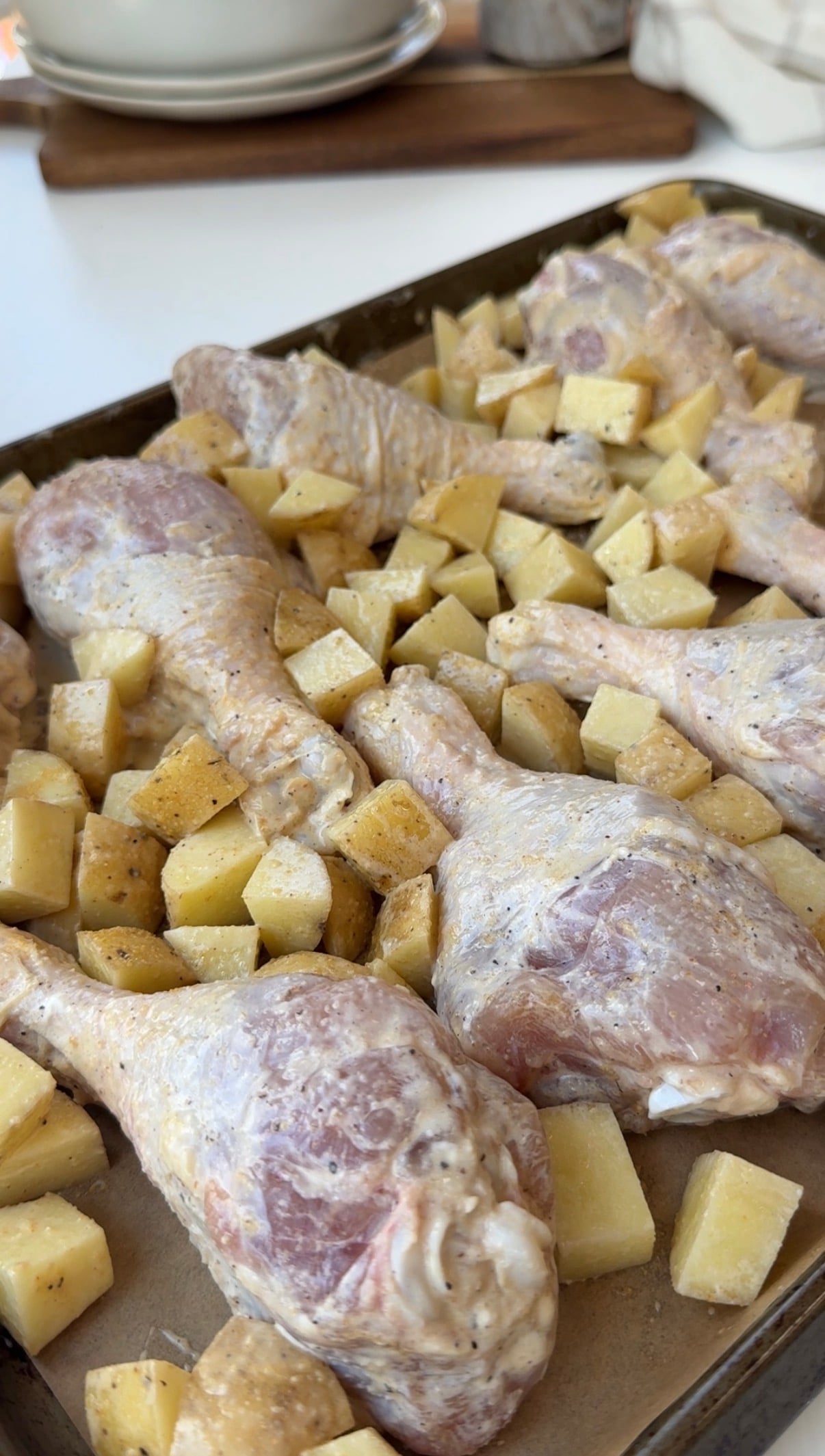 Raw, seasoned chicken drumsticks and diced potatoes arranged on a baking tray lined with parchment paper, ready to be cooked.