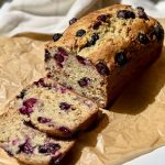 A loaf of blueberry banana nut bread with two slices leaning in front of loaf.