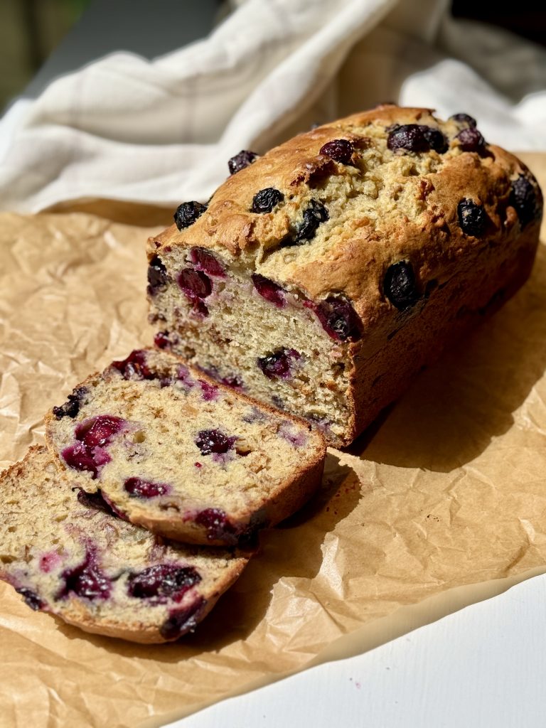 A loaf of blueberry banana nut bread with two slices leaning in front of loaf.