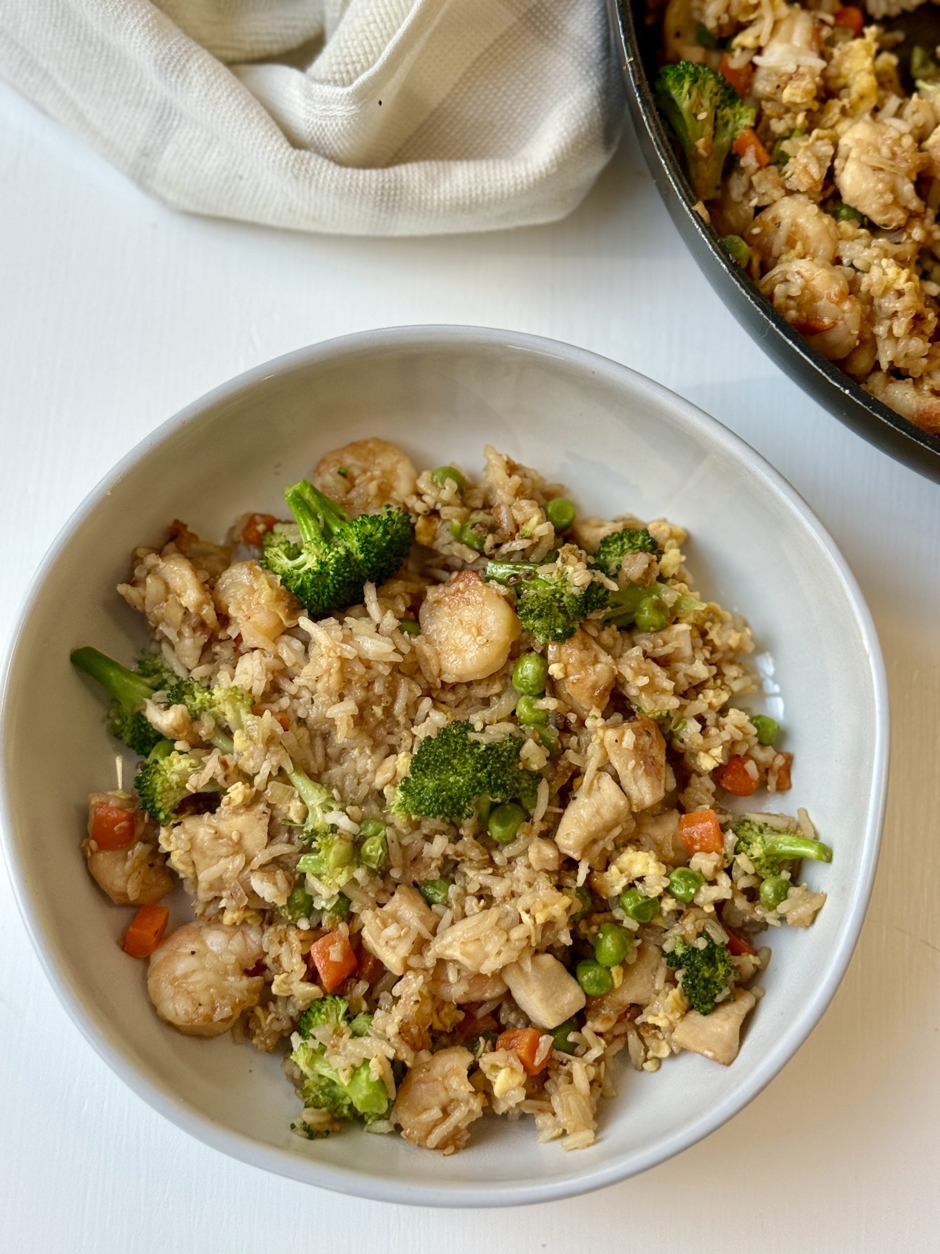 Chicken and shrimp fried rice in a bowl with a skillet of more to the side. 