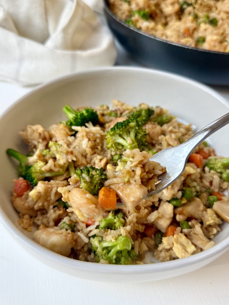 A bowl of shrimp and chicken fried rice with a fork holding up a bite.