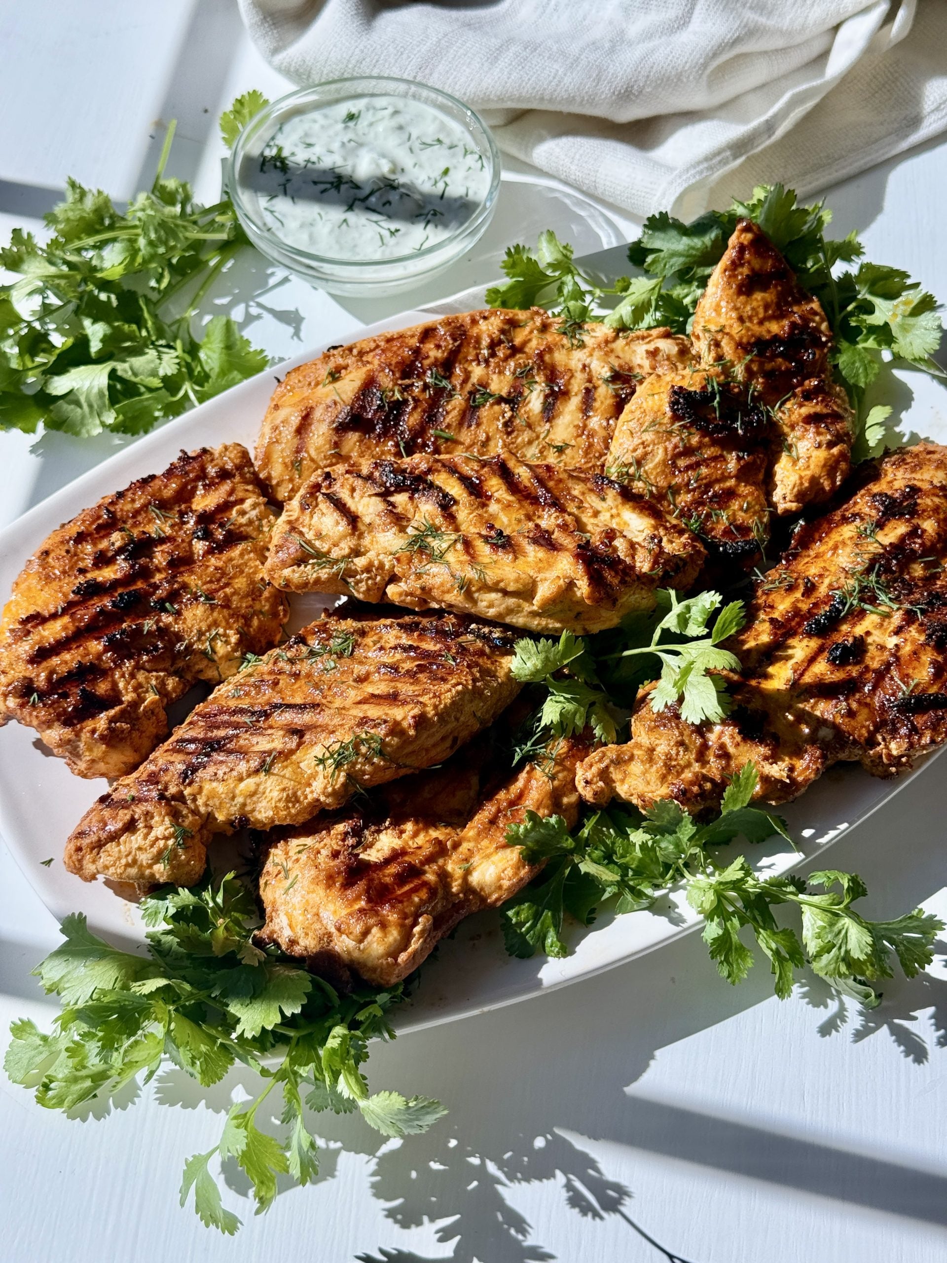 Chicken in a Greek yogurt marinade cooked and served on a platter with fresh herbs. 
