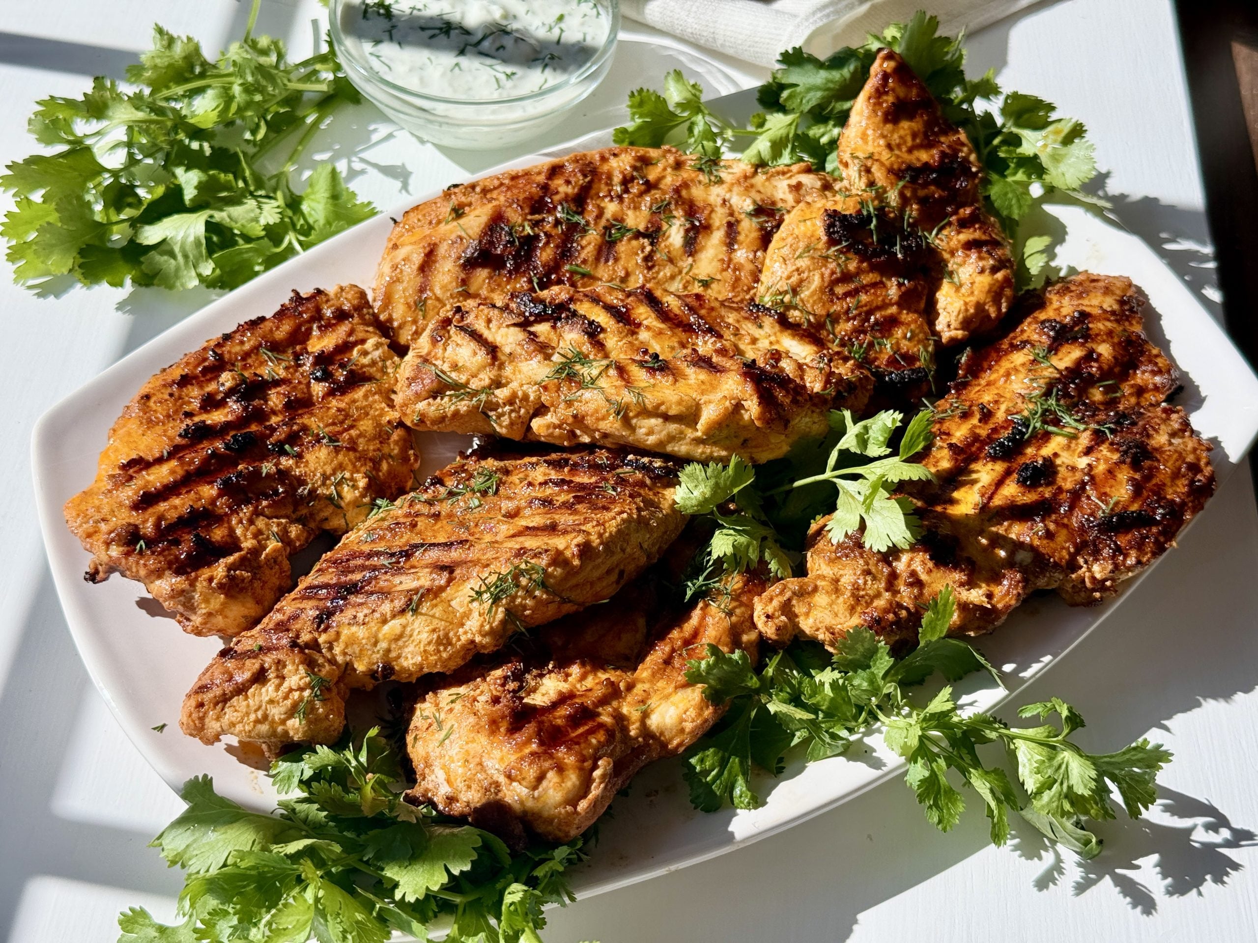 Greek yogurt marinated chicken on a white platter with herbs. 