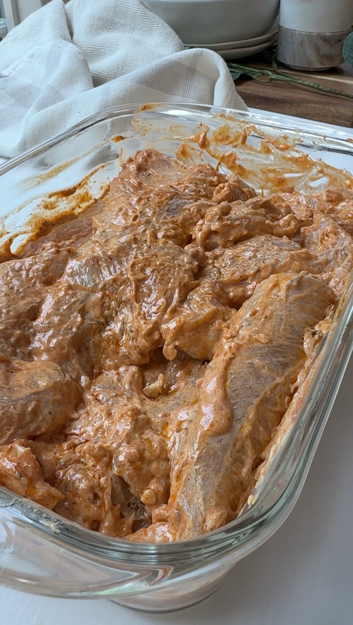 Chicken mixed into the yogurt marinade in a glass baking dish.