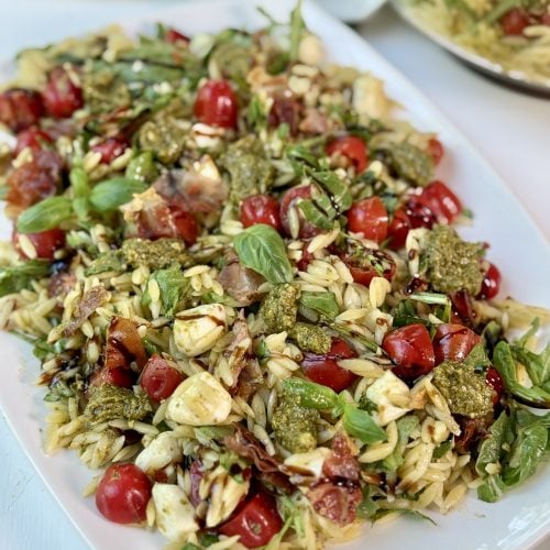 Pesto orzo pasta salad on a platter drizzled with balsamic glaze.
