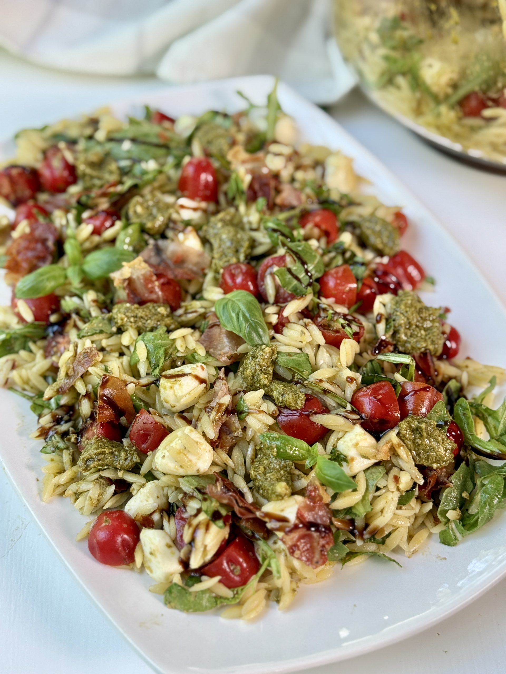 Pesto orzo pasta salad on a platter drizzled with balsamic glaze.