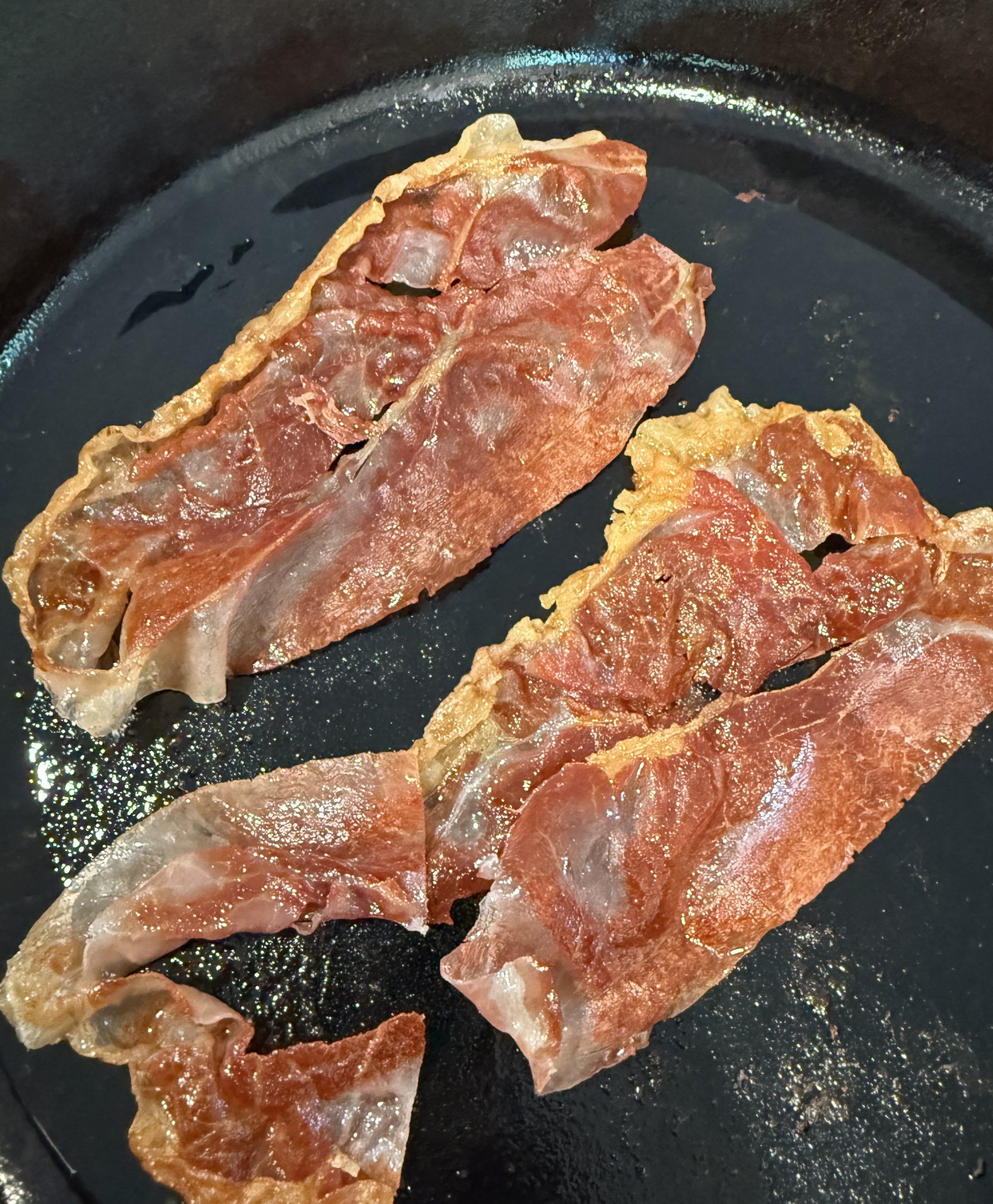 Slices of prosciutto cooking in a pan.