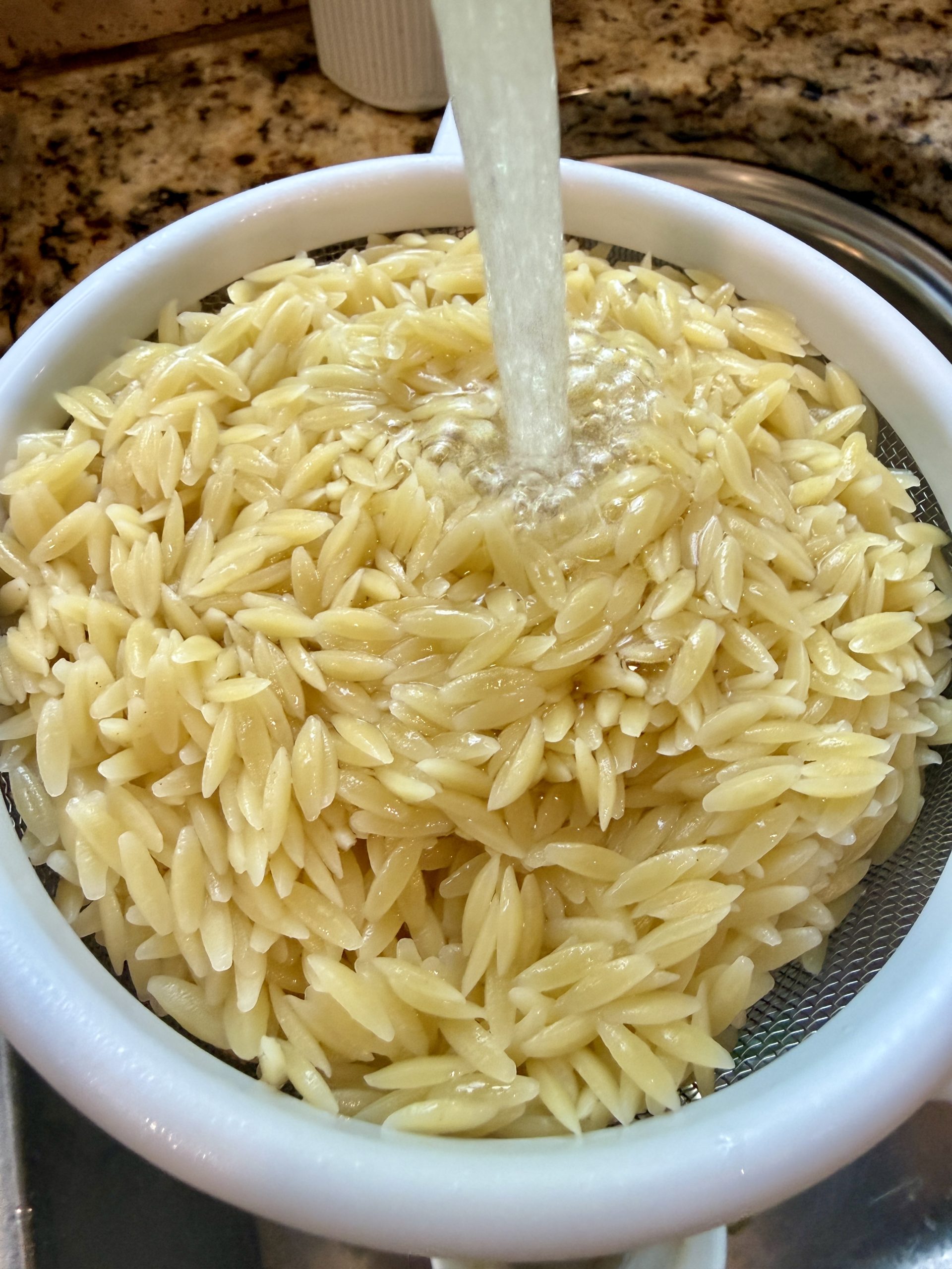 Orzo in a strainer with water pouring in.