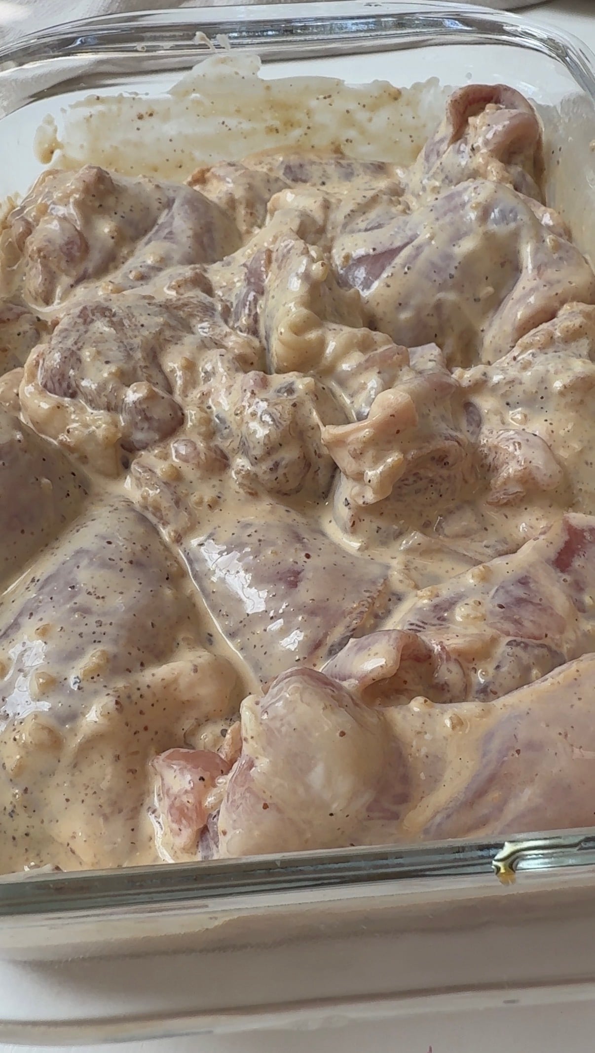 Raw chicken pieces coated in a creamy, seasoned marinade are arranged in a glass baking dish, ready for cooking.