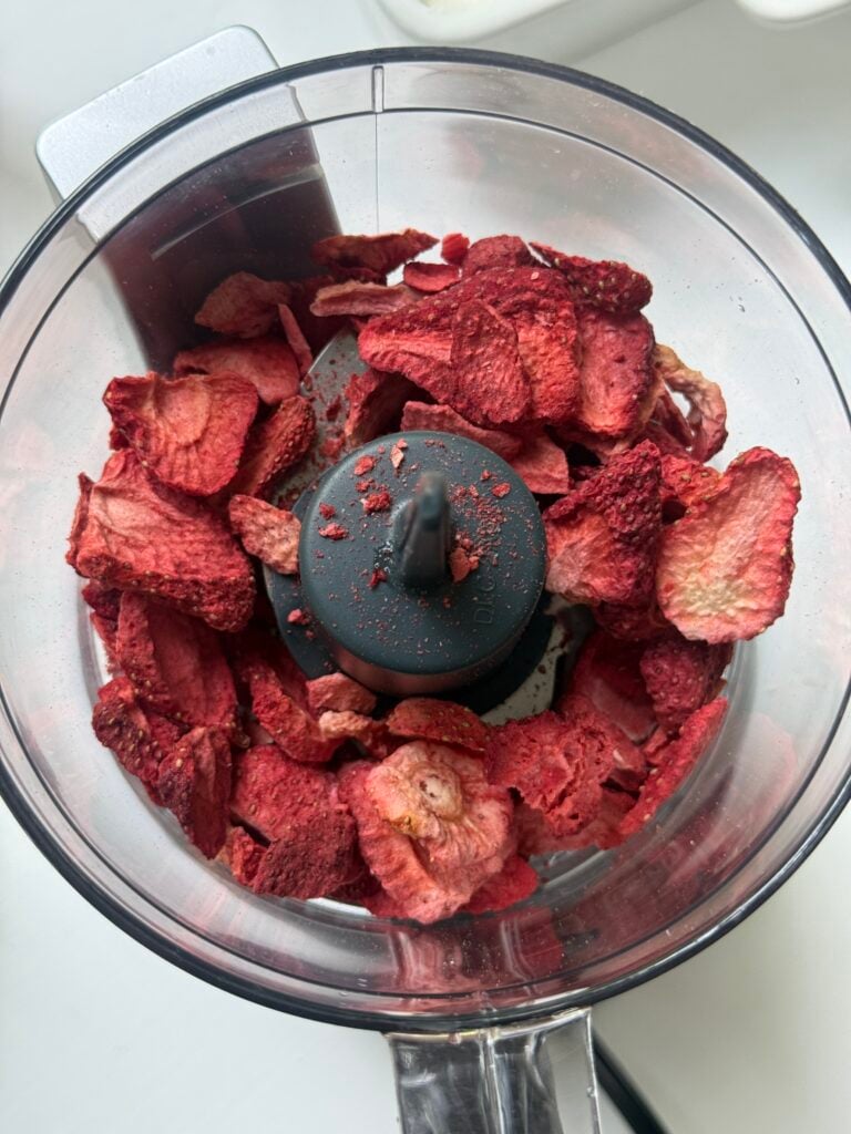 A food processor bowl filled with dried, sliced strawberries, ready to be blended.