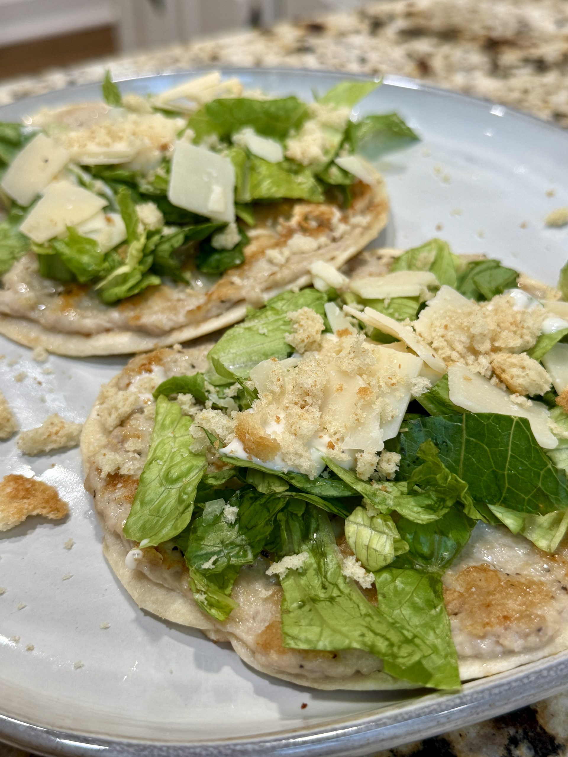 Two flour tortillas are being heated on a light-colored pan. The tortillas show slight browning in spots and appear to be lightly toasted. Some oil or melted butter is visible on the pans surface.