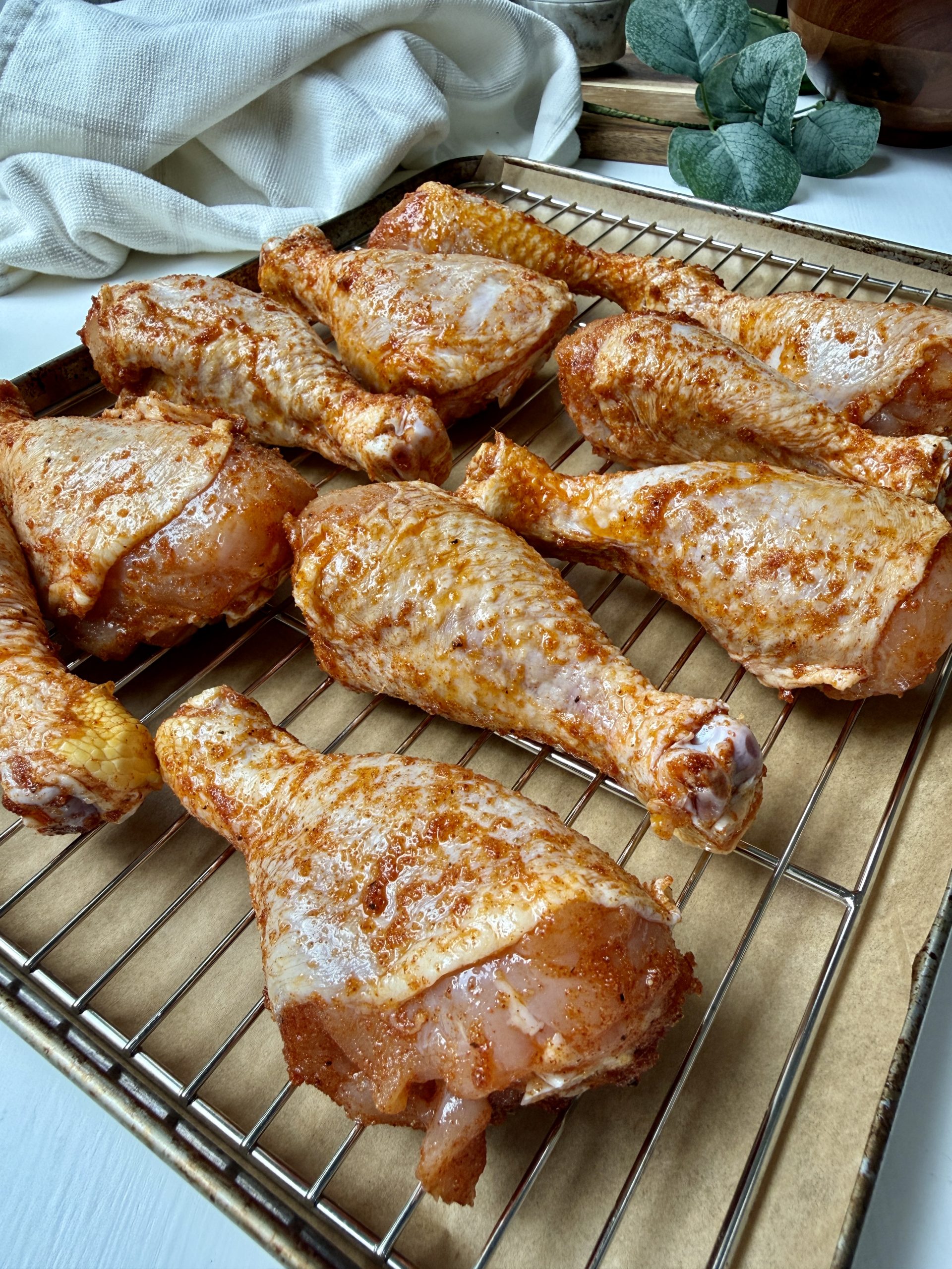 Chicken drumsticks with seasoning added to a baking rack.