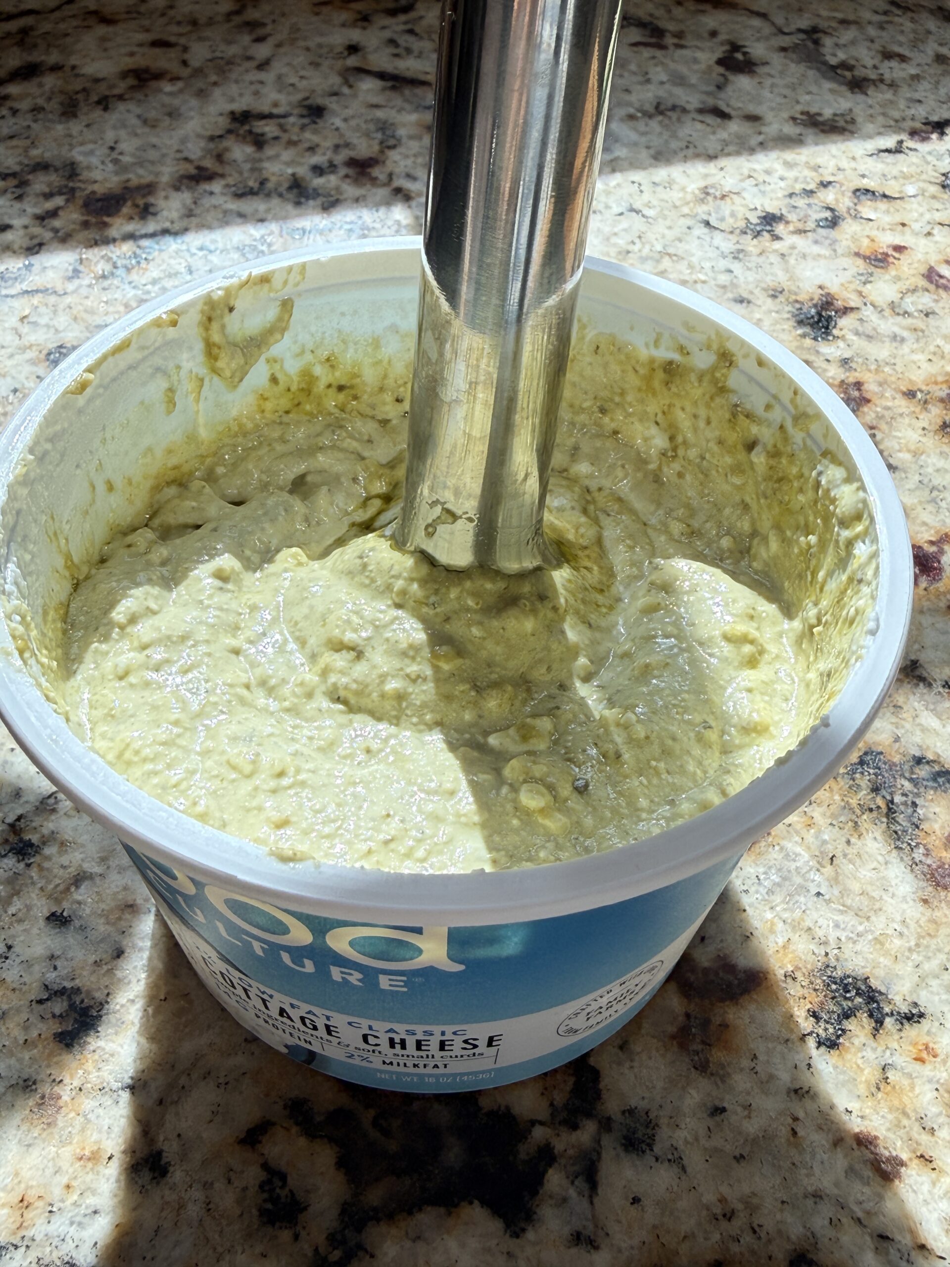 Blending the cottage cheese and pesto together with an immersion blender.