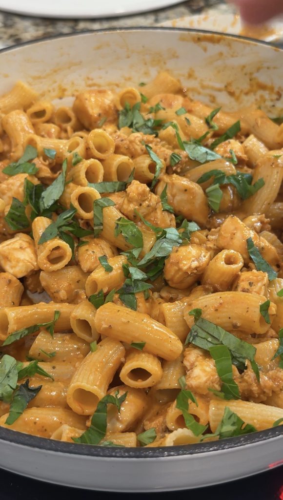 Chicken red pesto pasta in a skillet garnished with fresh basil. 
