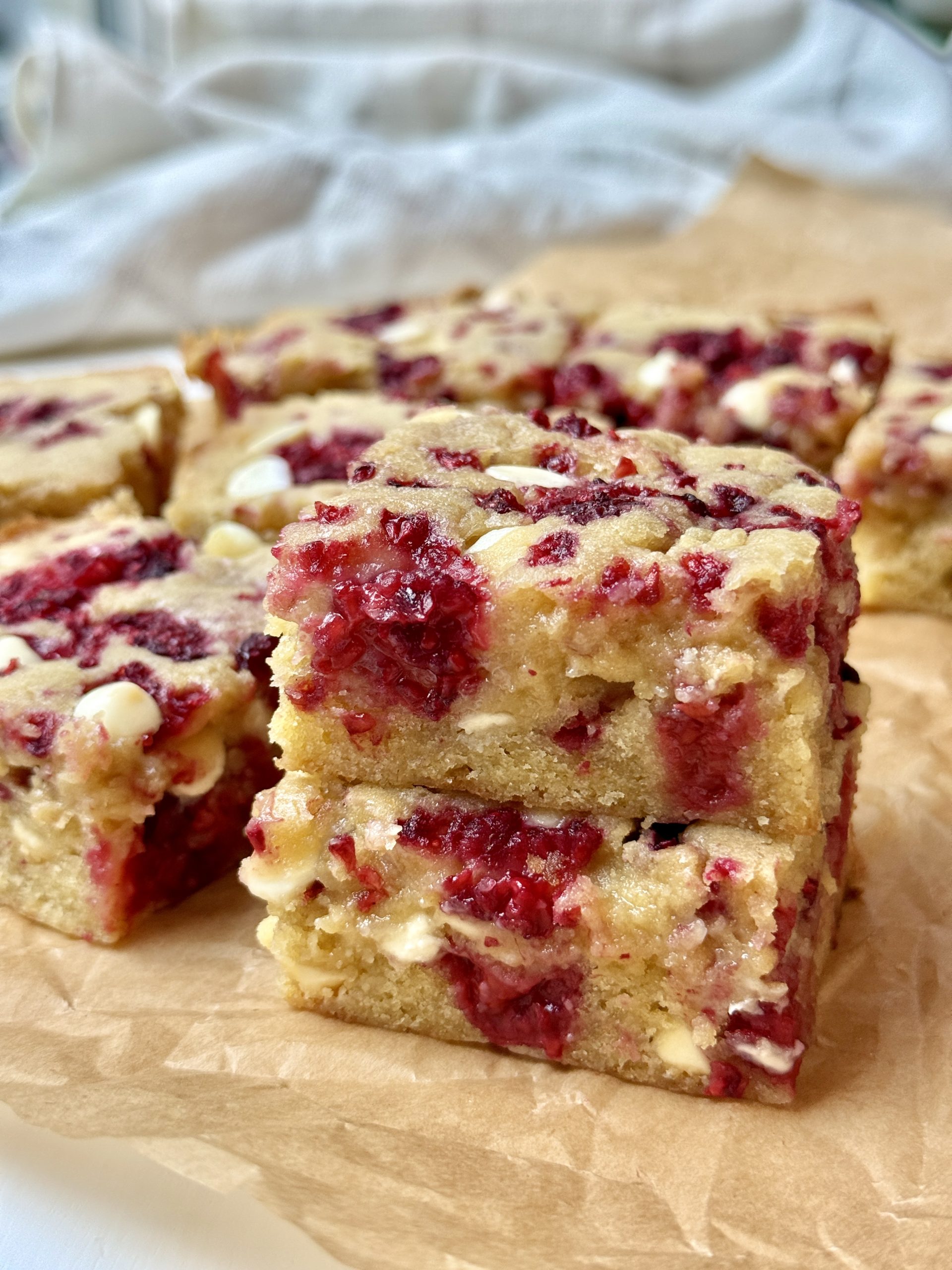 Two white chocolate raspberry blondies stacked on parchment with more in the background.