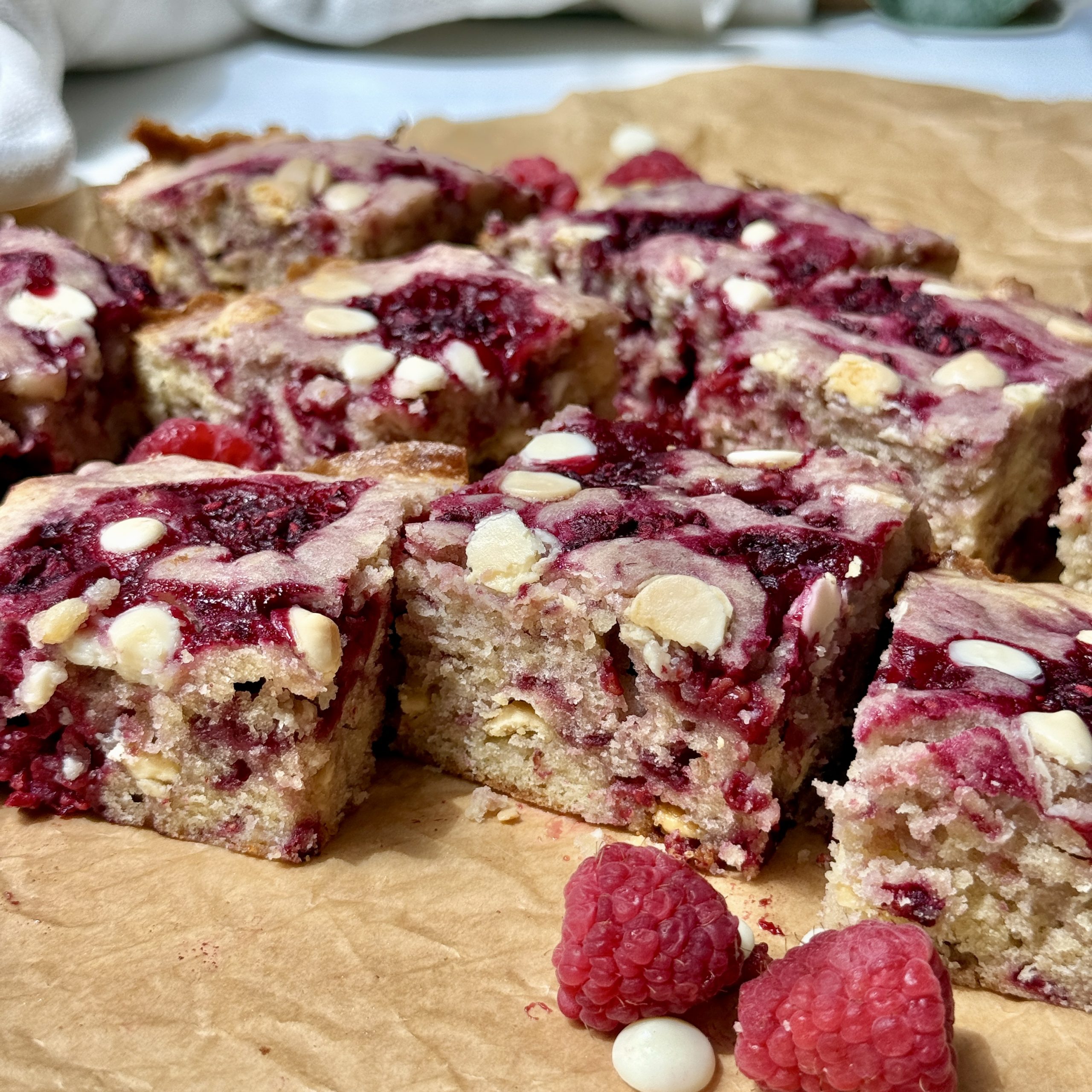 Sliced raspberry and white chocolate blondies on a piece of parchment.