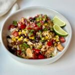 A bowl filled with rice, grilled chicken, black beans, corn, tomatoes, shredded cheese, cilantro, and two lime wedges.