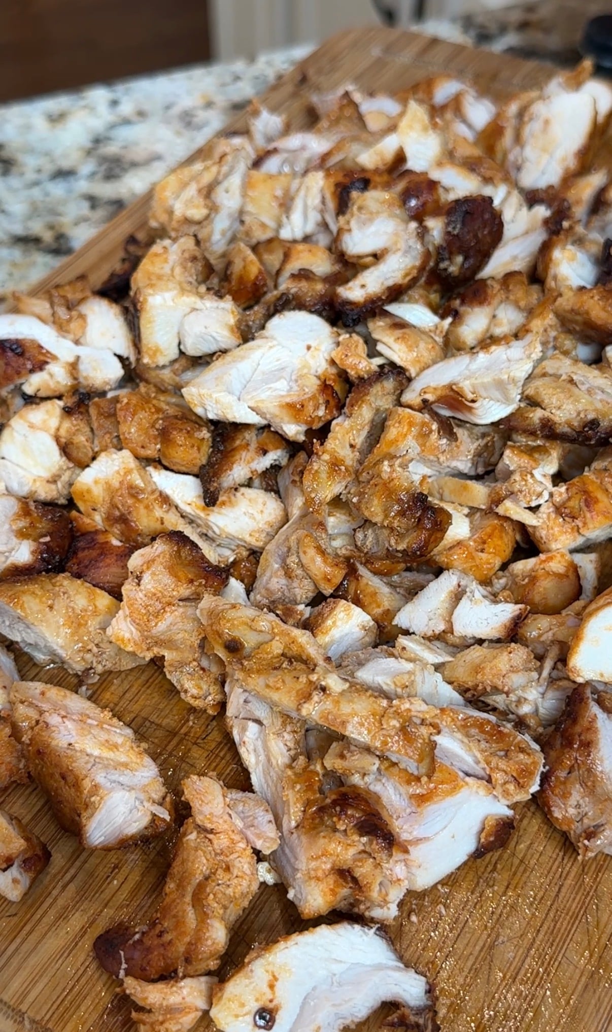 Chopped, grilled chicken pieces on a wooden cutting board, showing a mix of white meat and crispy, seasoned edges.