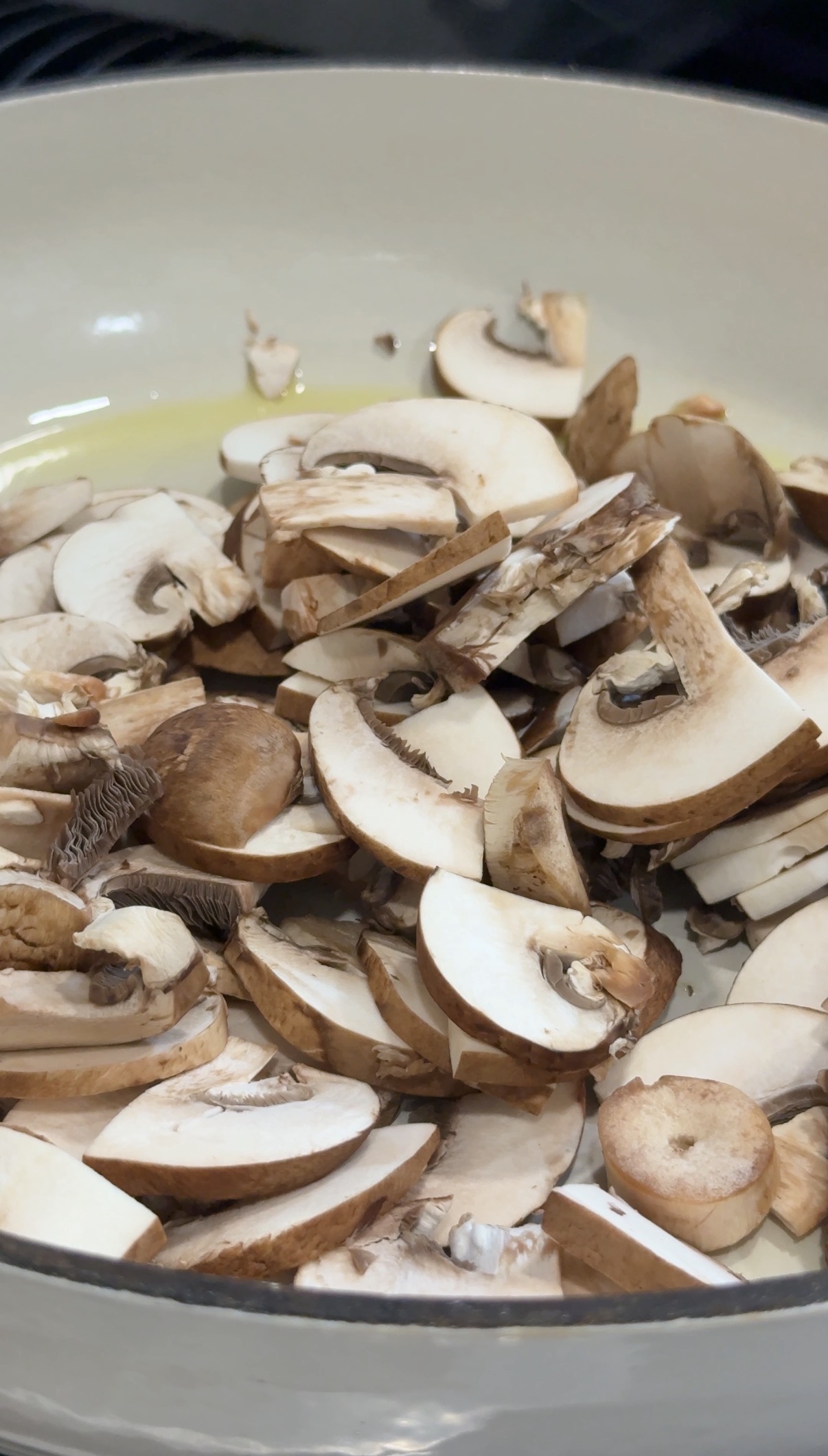 A close-up of a pile of raw, sliced mushrooms in a bowl, showing their light brown caps and white stems.