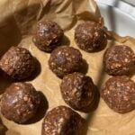Nine round chocolate oat energy bites on brown parchment paper in a white dish, with sunlight casting soft shadows.