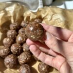 round chocolate oat energy bites on brown parchment paper in a white dish, with sunlight casting soft shadows.