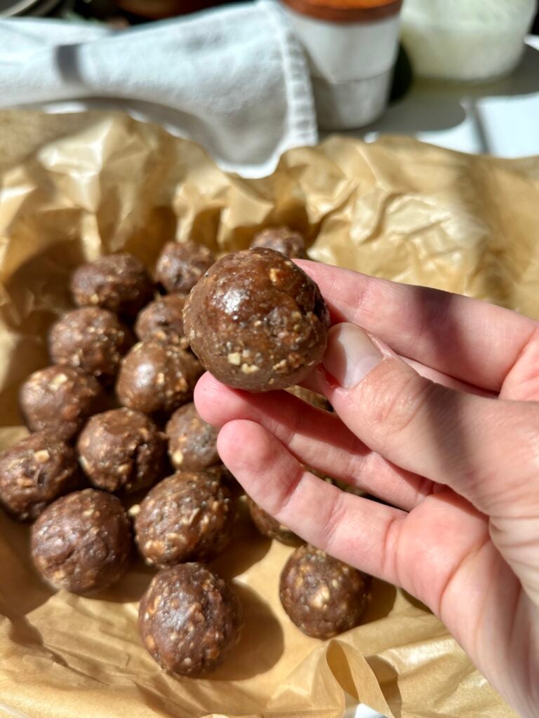 round chocolate oat energy bites on brown parchment paper in a white dish, with sunlight casting soft shadows.