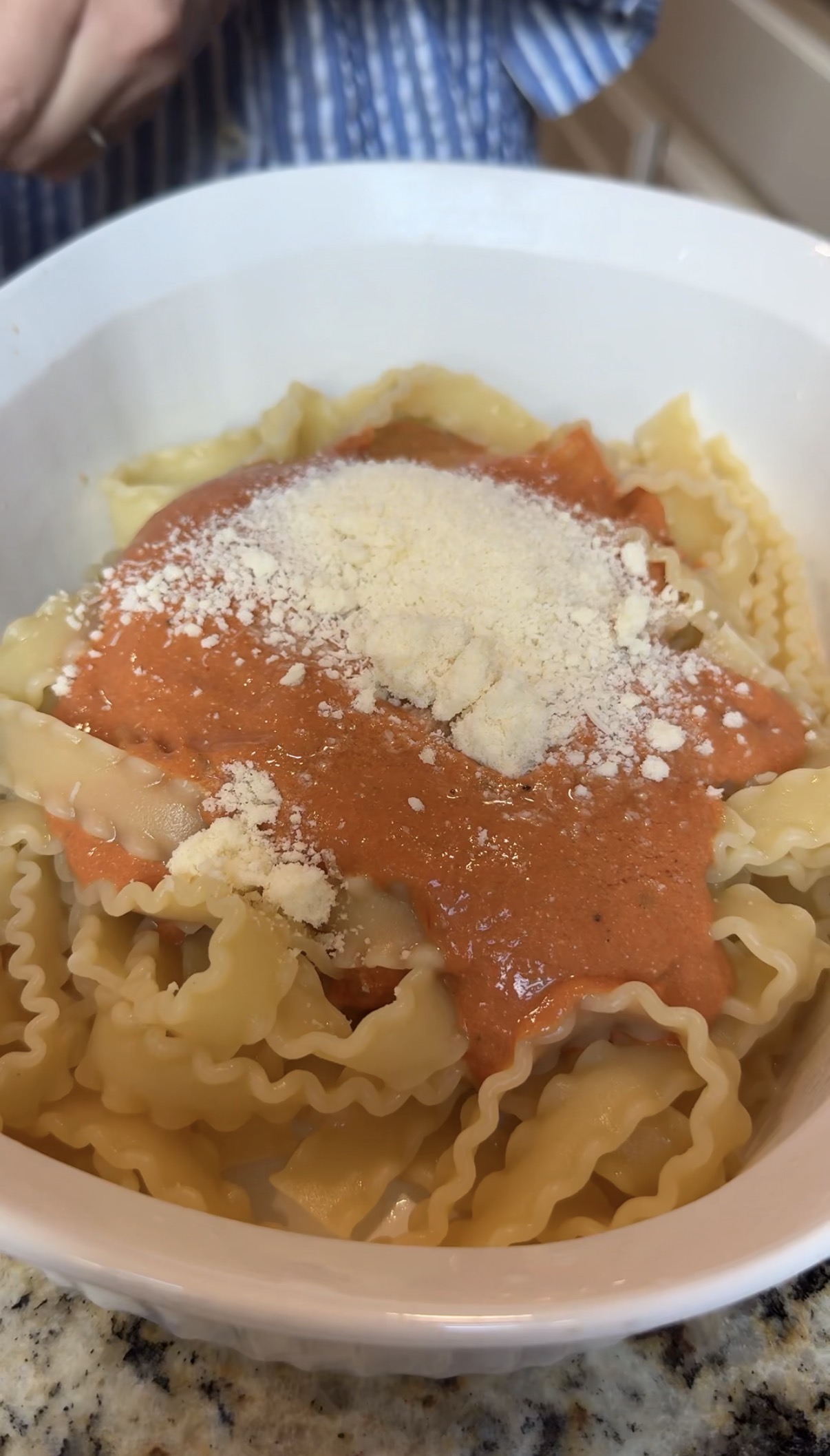 Wavy-edged pasta in a white bowl topped with creamy red tomato sauce and a sprinkle of grated parmesan cheese.