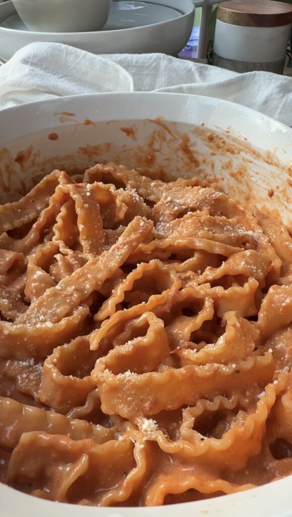 Wavy-edged pasta covered in creamy tomato sauce, topped with grated cheese, served in a white bowl.