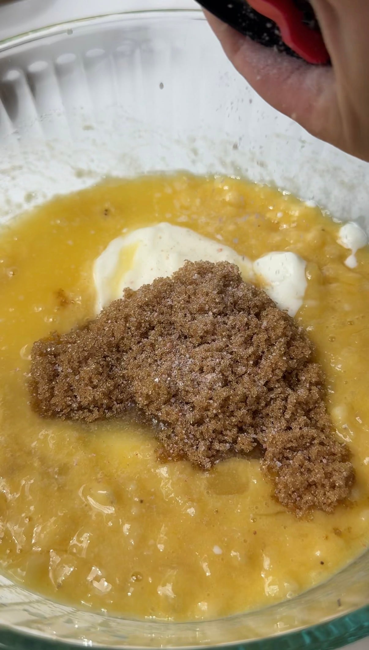 A close-up of a mixing bowl with mashed bananas, brown sugar, and a dollop of sour cream about to be mixed together.