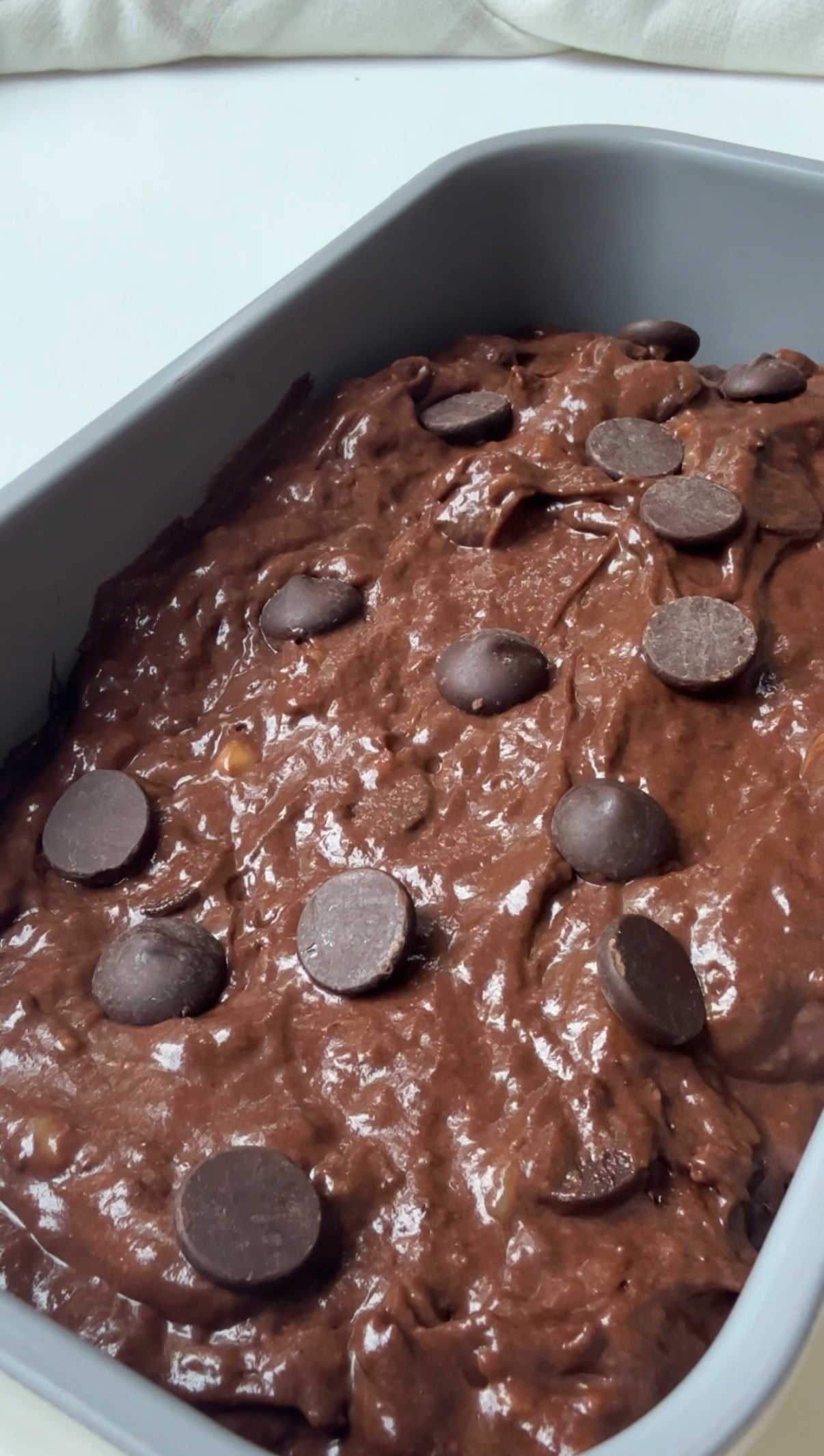 A close-up of unbaked chocolate brownie batter in a pan, topped with scattered chocolate chips.