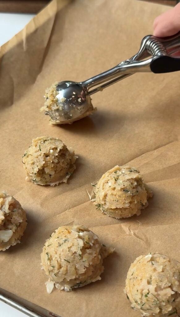 An ice cream scoop forms balls of a crumbly, seasoned mixture on parchment paper, ready for baking.