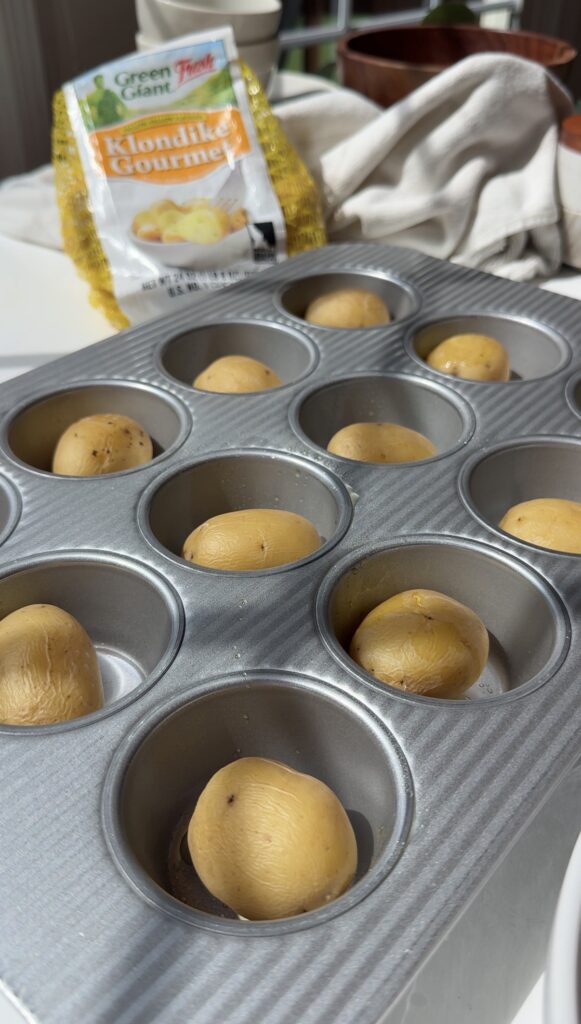 A muffin tin with small yellow potatoes placed in each cup. A bag labeled Klondike Gourmet and a towel are in the background.