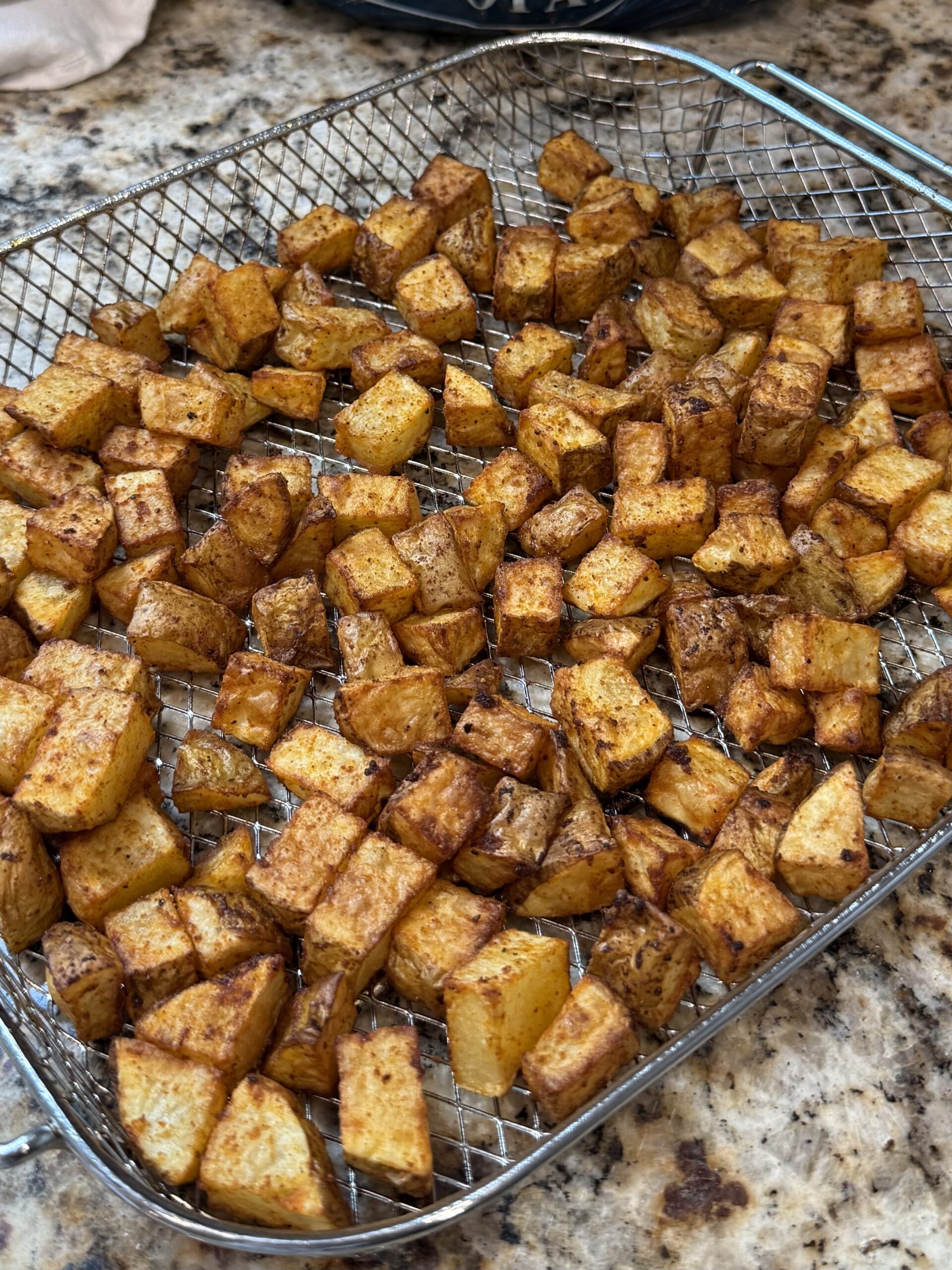 Diced, seasoned chicken pieces are sizzling in a black cast iron skillet on a stovetop, with steam rising and a granite countertop visible in the background.