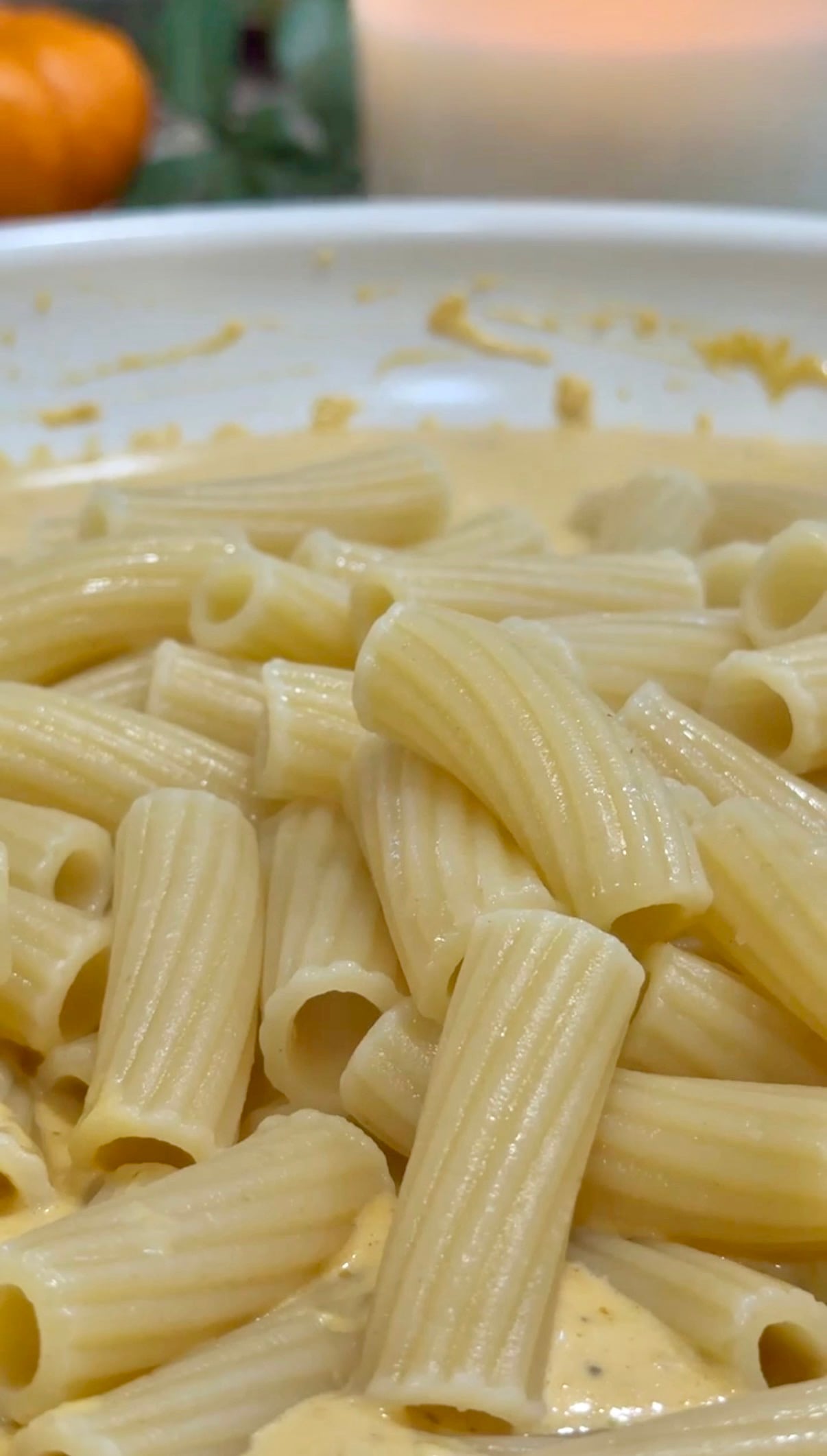 Close-up of rigatoni pasta coated in a creamy yellow sauce, served in a white dish. The pasta appears freshly cooked and glossy, with sauce lightly covering the surface.