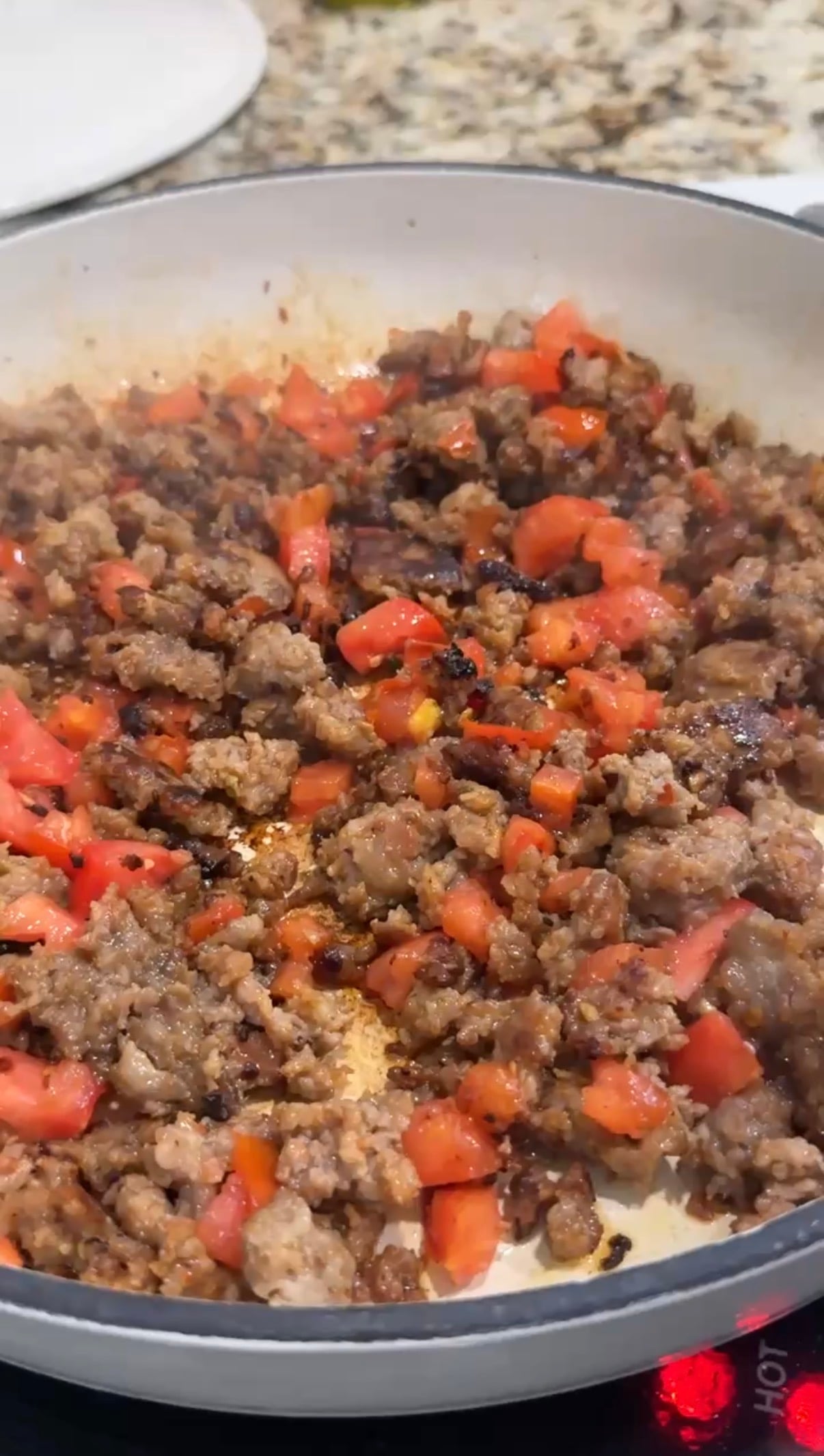 Ground meat is browning in a skillet with a pile of freshly chopped tomatoes added on top, ready to be mixed in and cooked together.