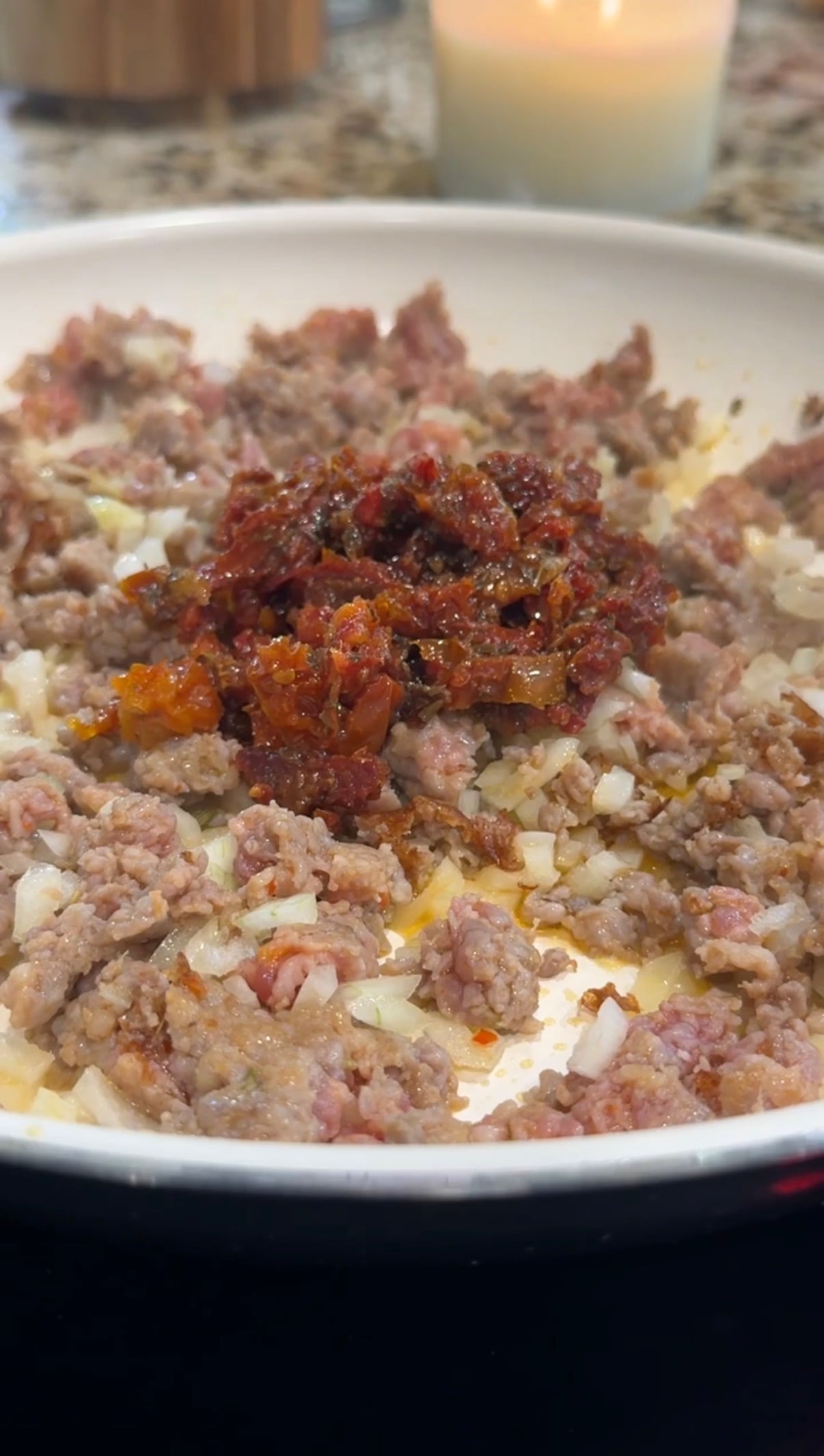 Ground meat and diced onions are cooking in a skillet, with chopped sun-dried tomatoes piled in the center.
