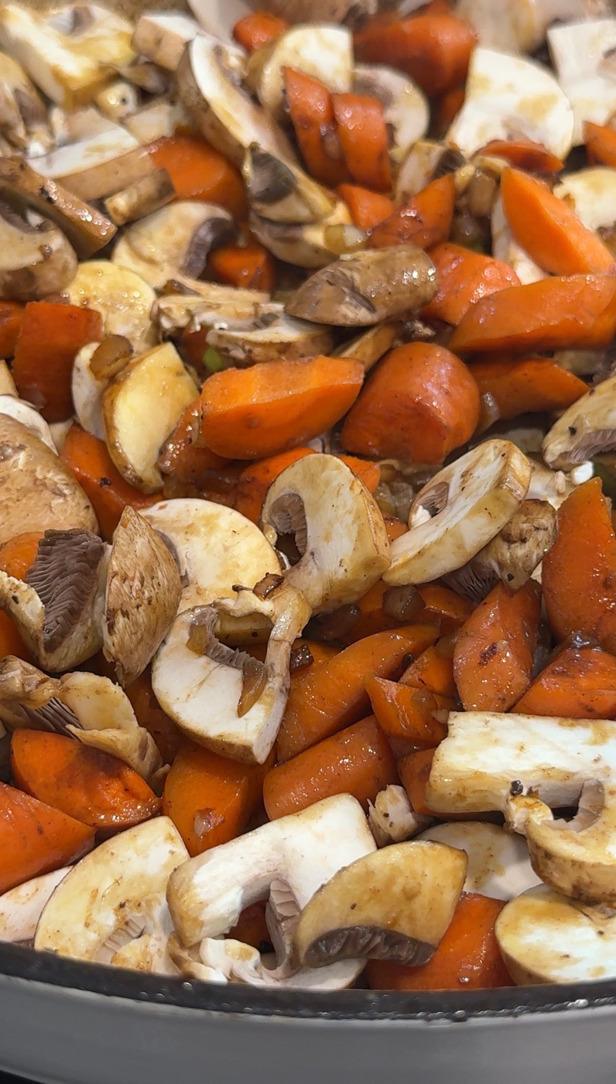 Chopped carrots and mushrooms are mixed together in a pan, showing a combination of orange and brown colors, likely being sautéed or prepared for cooking.