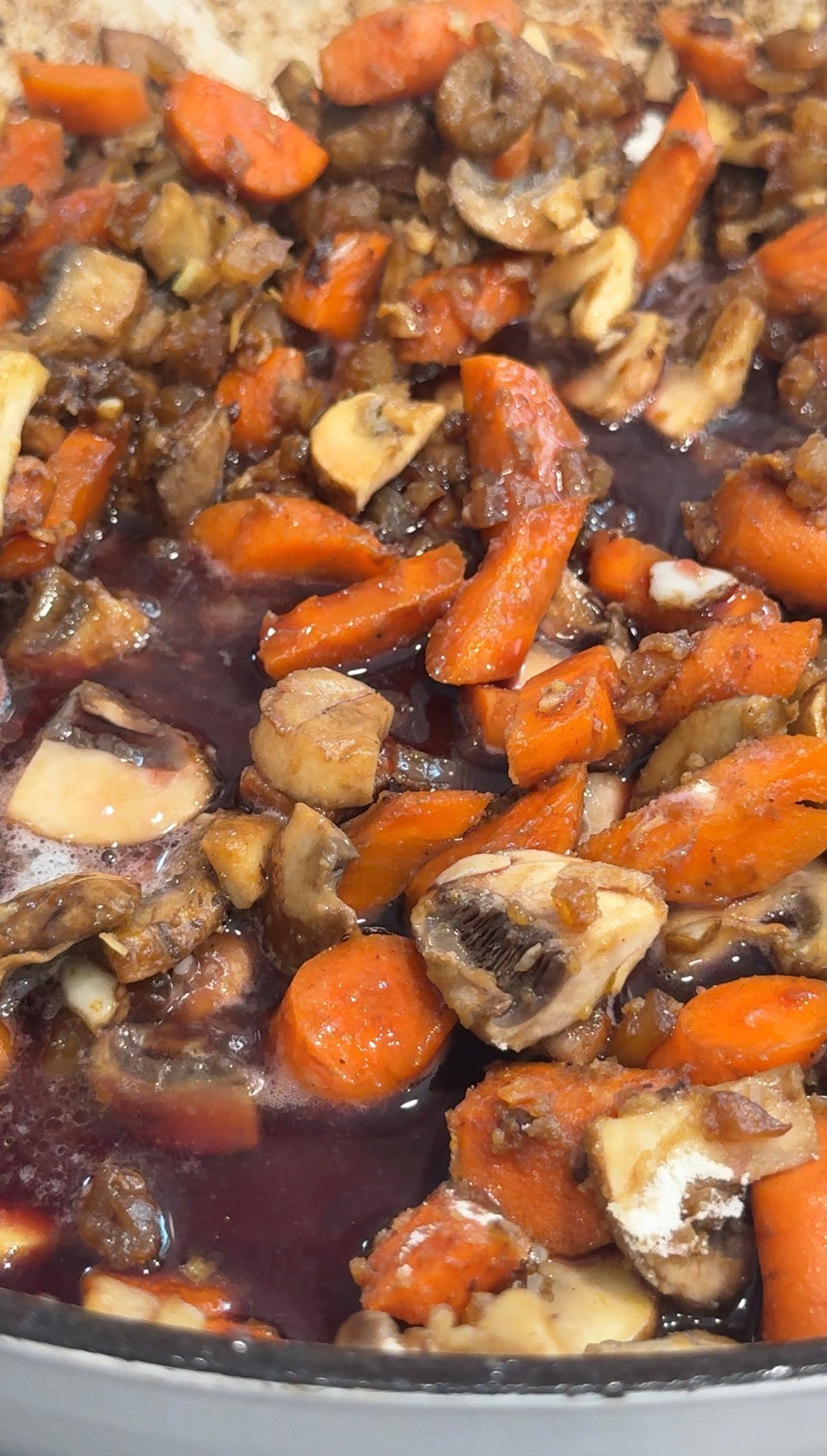 Chopped carrots and mushrooms simmer in a reddish-brown liquid, possibly a stew or sauce, creating a hearty, colorful mixture.