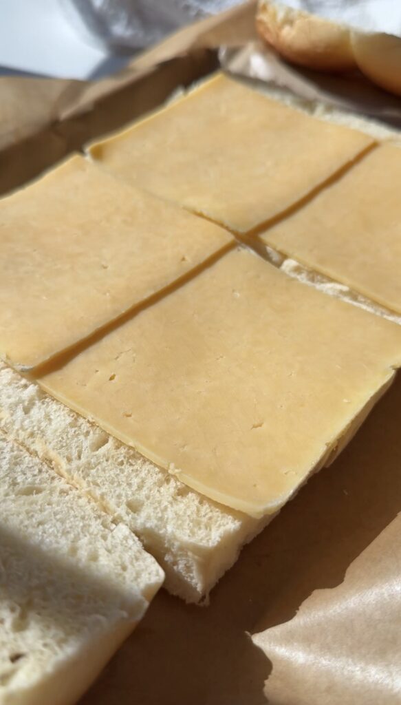 Four slices of yellow cheese are neatly placed on top of a piece of white bread, with the bread and cheese both cut into four squares.