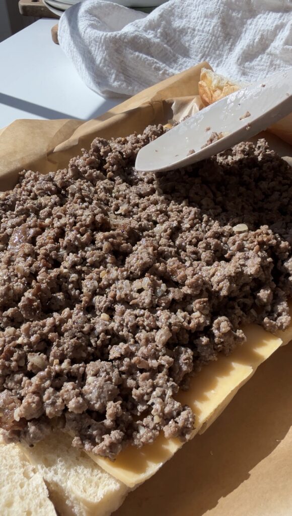 Cooked ground beef is being spread onto buns with a spatula on parchment paper.