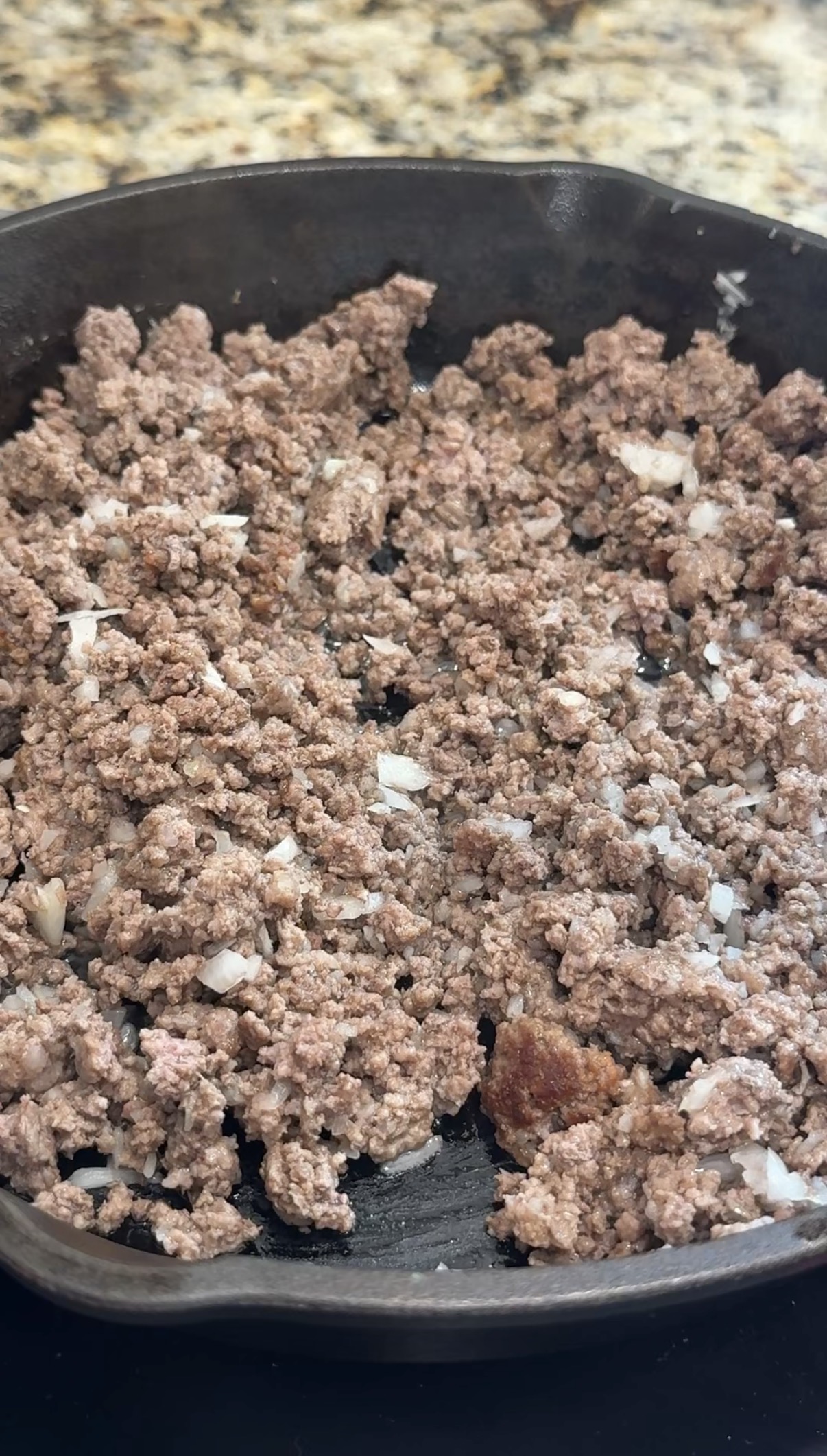 Ground beef and chopped onions cooking in a skillet, with the meat browned and the onions partially softened.