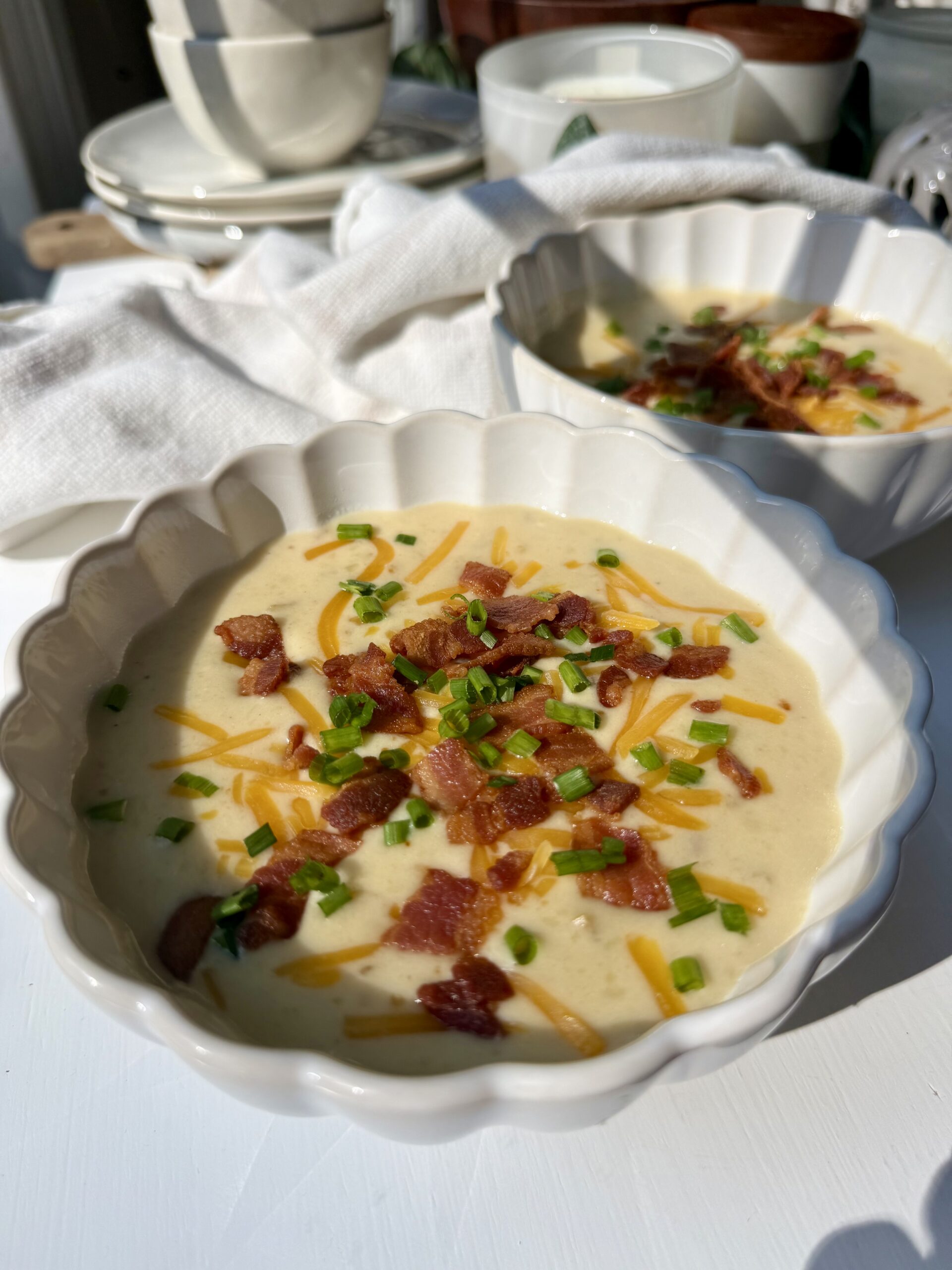 Loaded baked potato soup in two ceramic bowls topped with cheddar cheese, crispy bacon, sour cream, and green onions