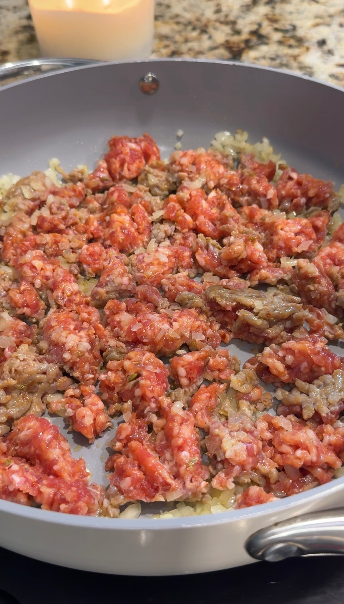 Italian sausage and diced onion cooking in a large skillet