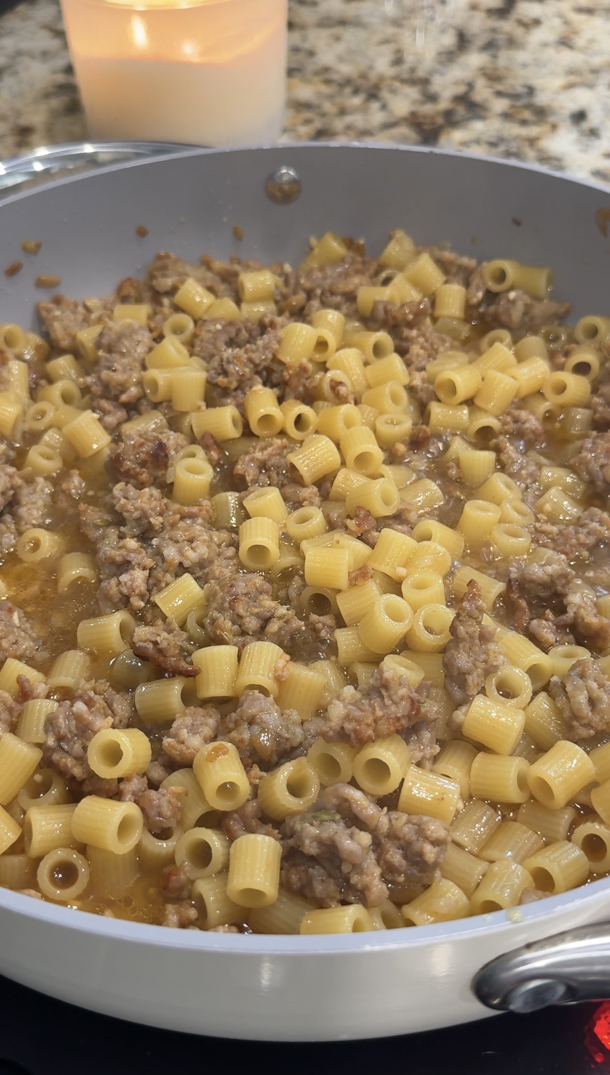 Ditalini pasta simmering with Italian sausage and broth in a skillet