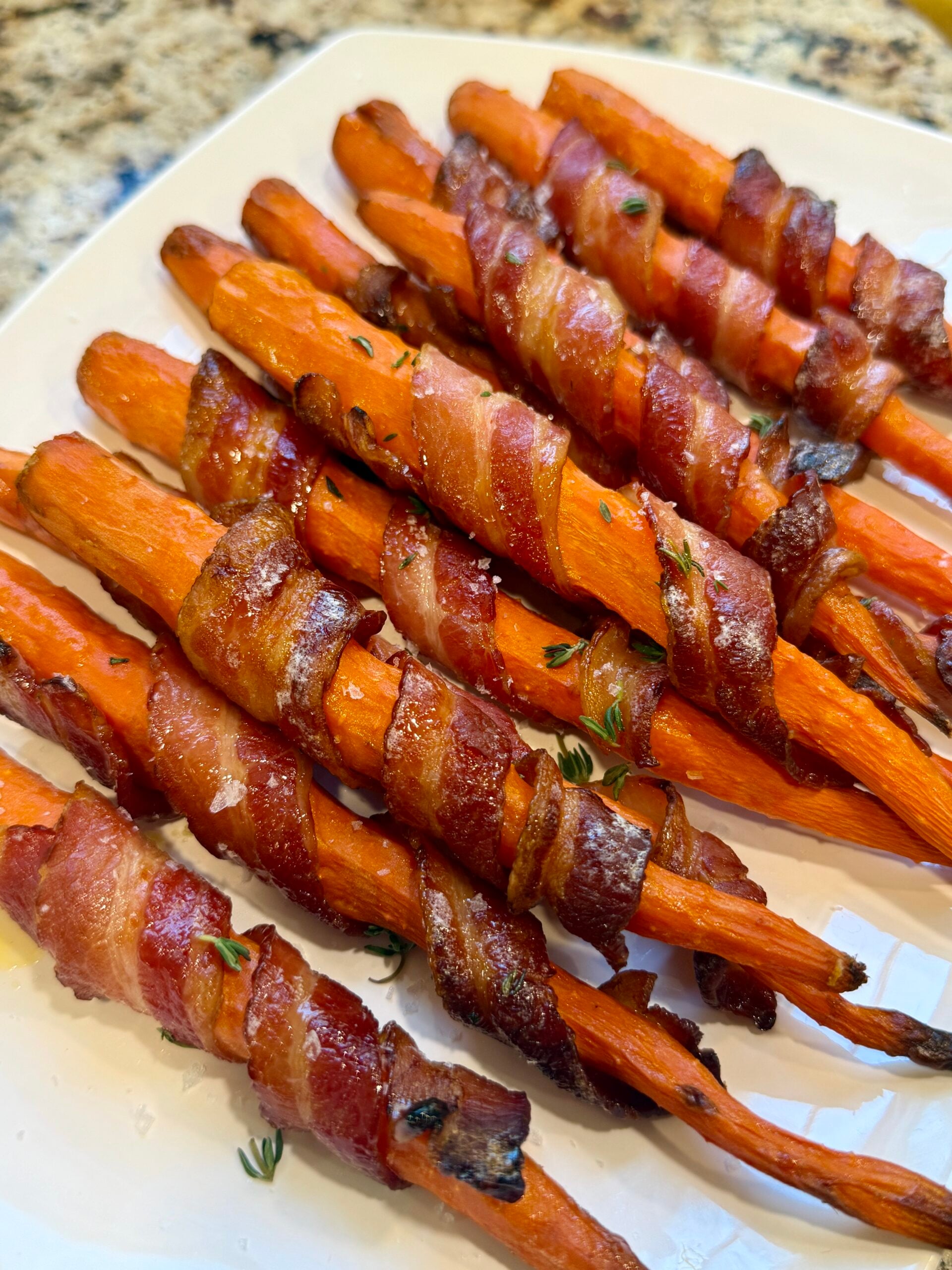 Carrots wrapped in bacon, cooked and laid out on a white platter