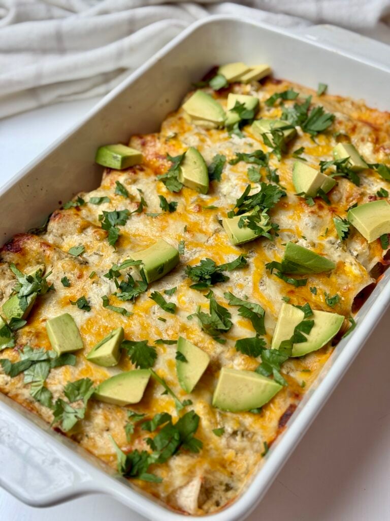 A white baking dish of chicken enchiladas with sour cream.