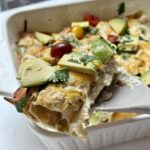 A spatula holding up a serving of chicken enchiladas with sour cream.