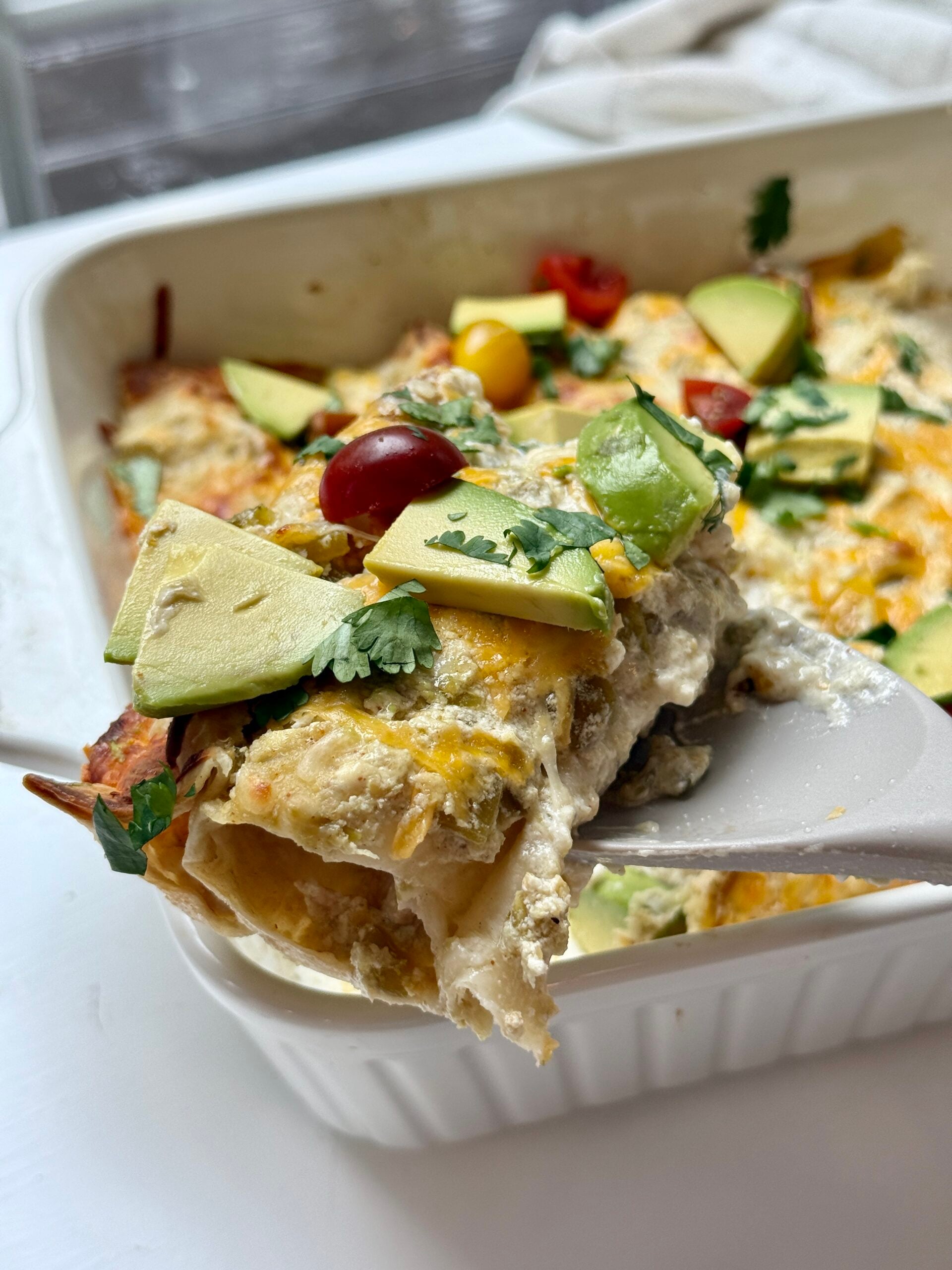 A spatula holding up a serving of chicken enchiladas with sour cream.